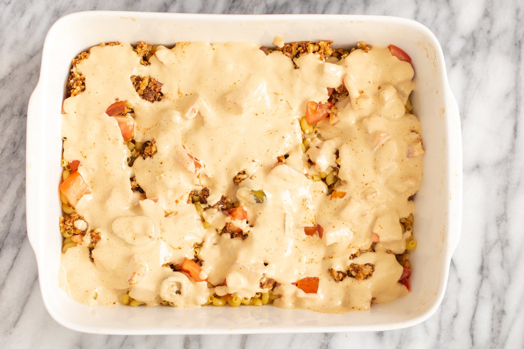 vegan queso sauce being poured over mac and cheese taco casserole