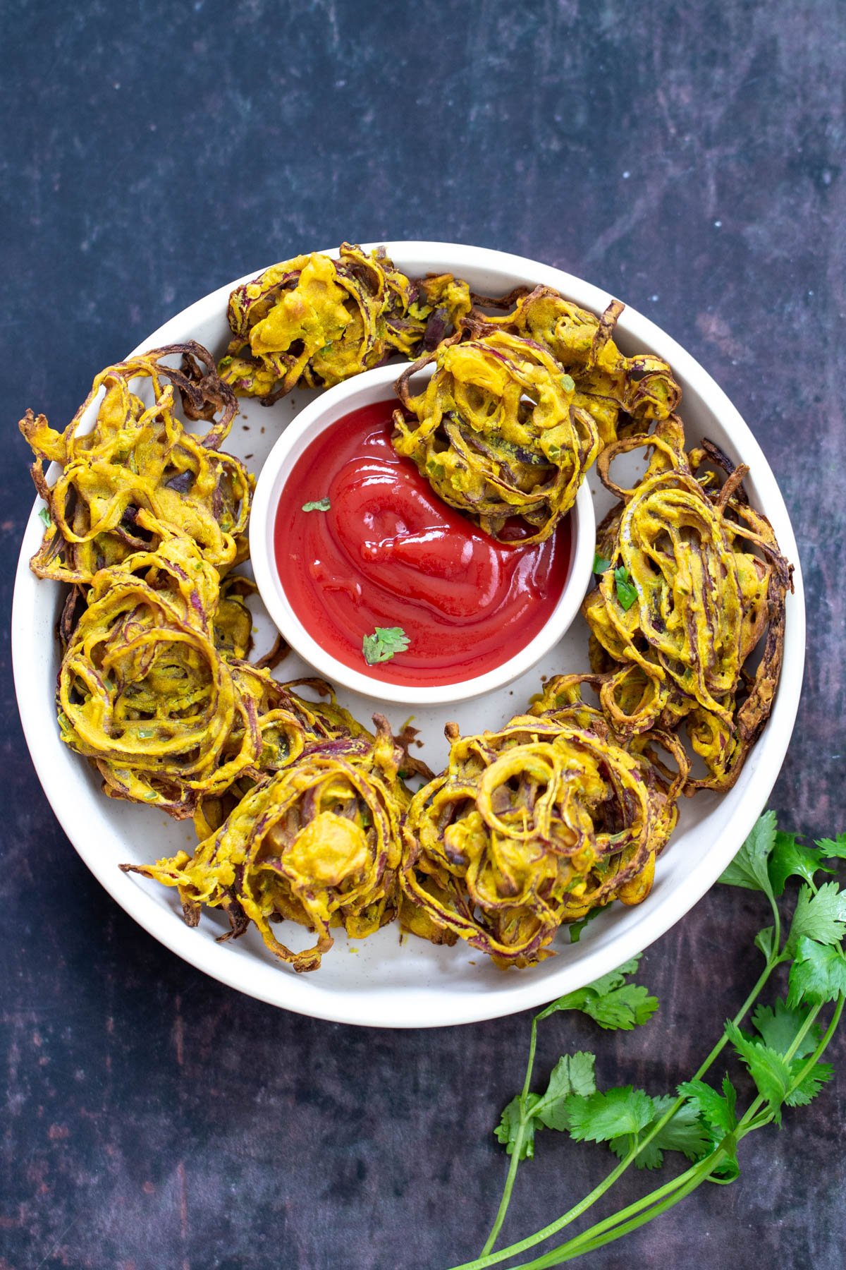 baked pakora  baked vegan onion bhaji arranged on a white platter with a small dish of ketchup in the middle