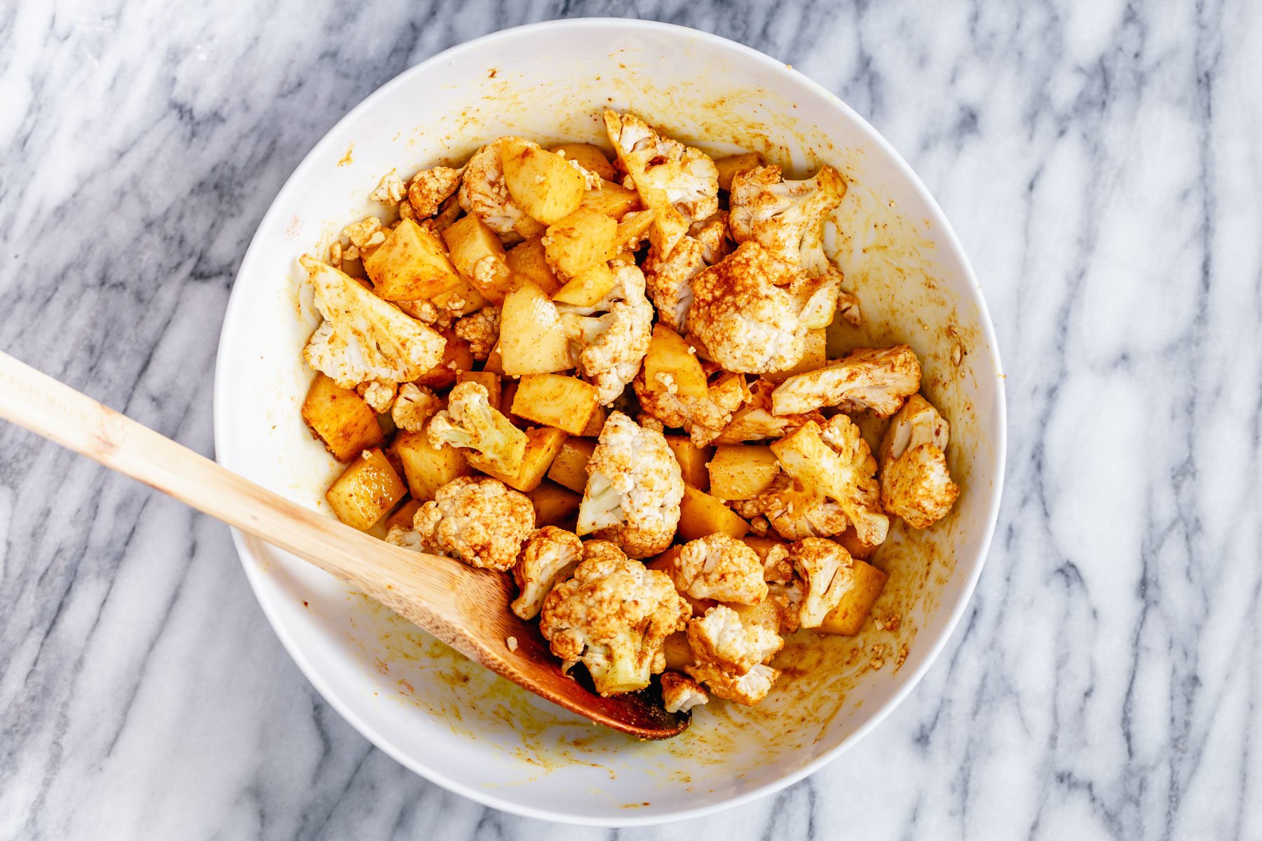 vegan aloo gobi a white bowl with cauliflower and potato cubes being tossed with Indian spices