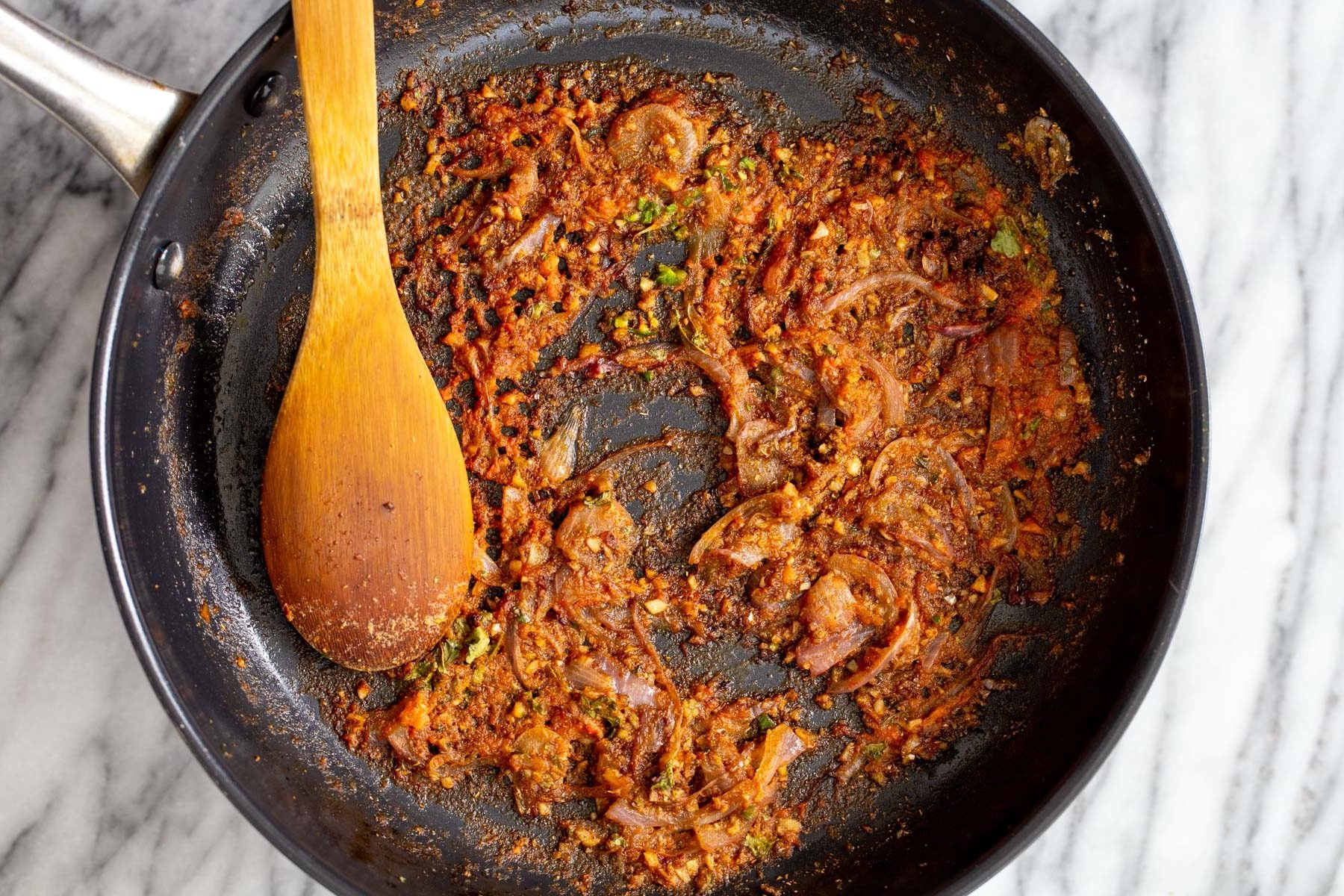 vegan aloo gobi onion and garlic being sauteed with spices and tomato puree in a black frying pan