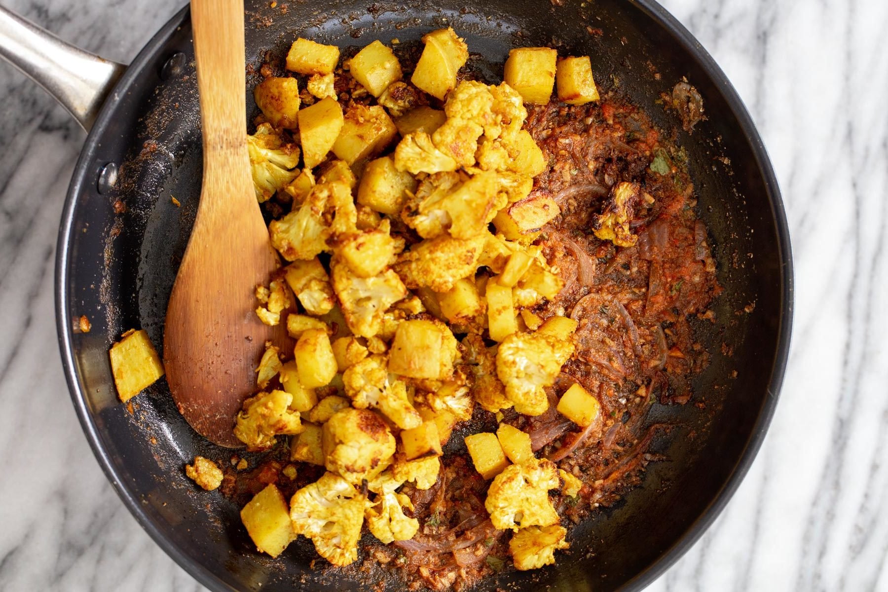 vegan aloo gobi  cauliflower and potato cubes being tossed with sauteed spices