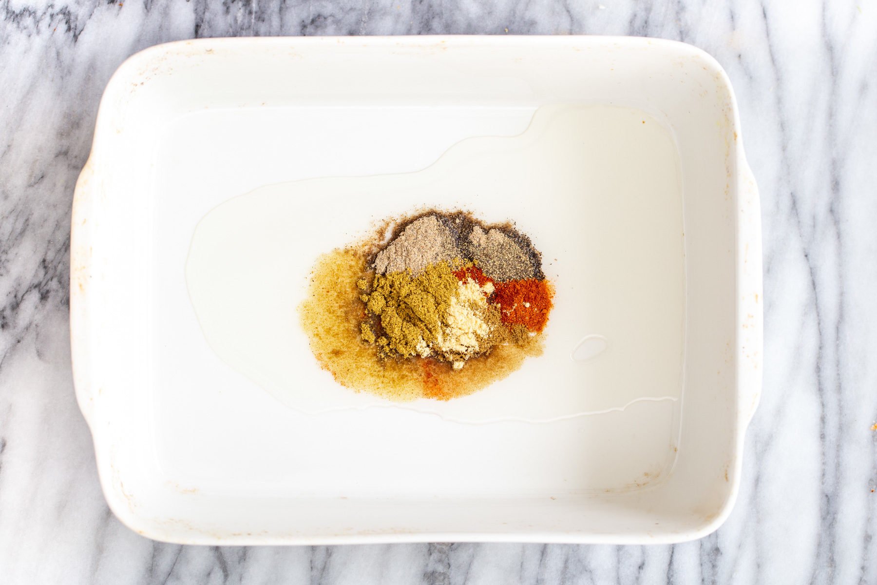 Vegan Vegetable Casserole oil and indian spices in a white casserole dish