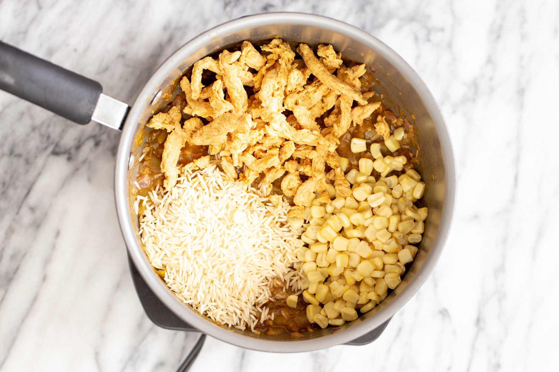 vegan enchilada soup  rice, soy chunks and corn being added to a pot with vegan enchilada soup