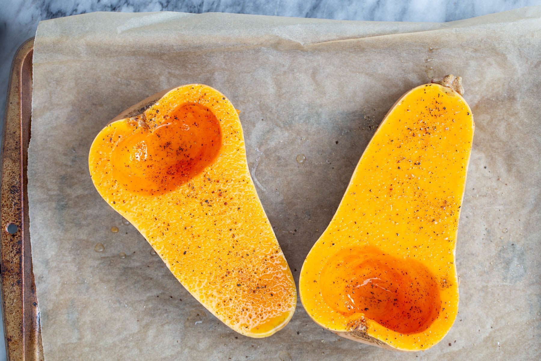 vegan stuffed butternut squash 2 butternut squash halves on a baking sheet drizzled with oil and sprinkled with salt and pepper