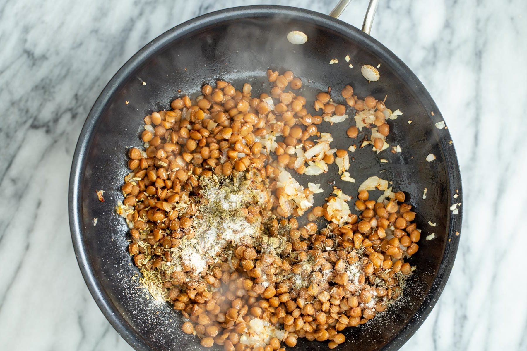vegan stuffed butternut squash lentil onion stuffing mixture and spices sauteeing in a frying pan