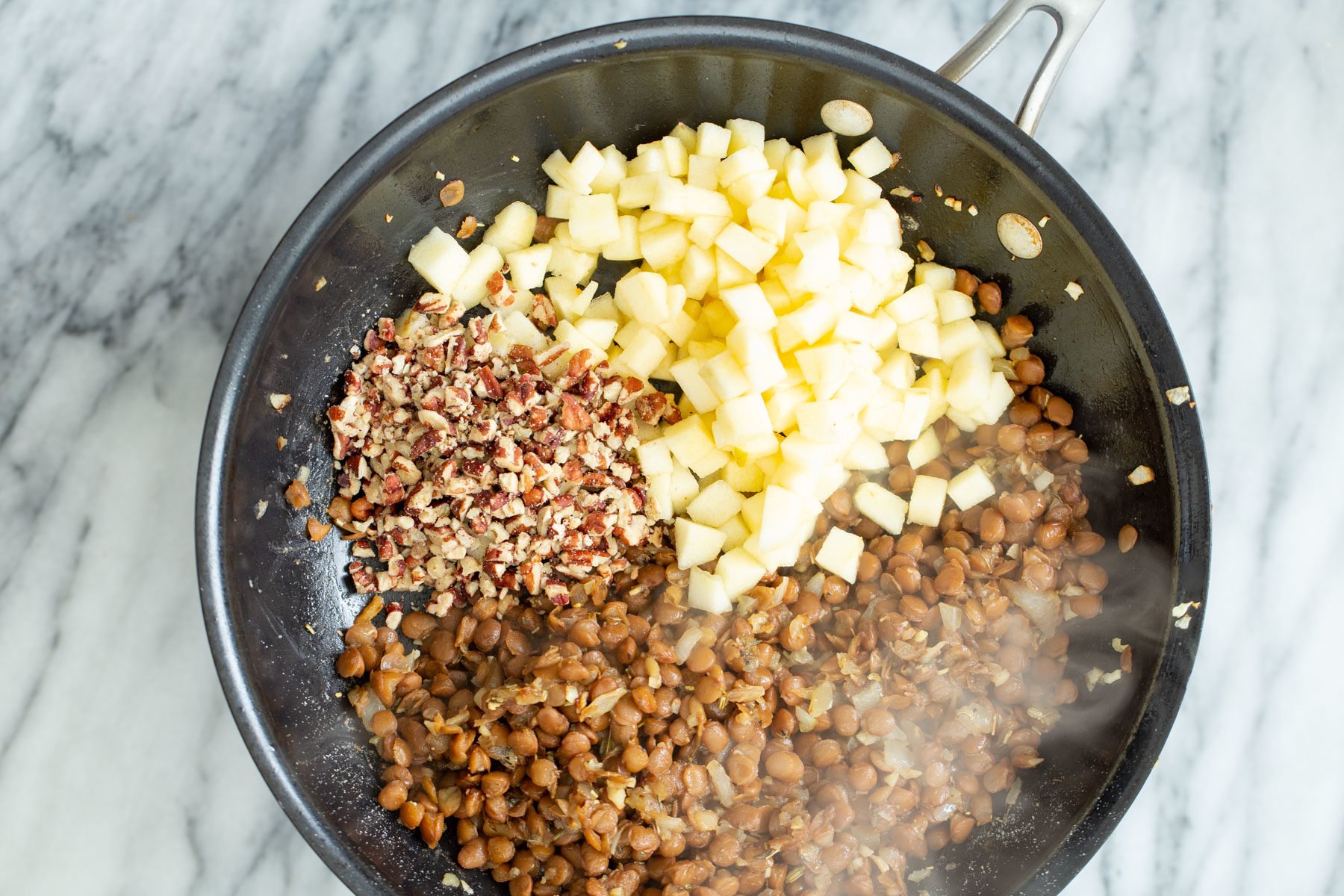 vegan stuffed butternut squash  apples and chopped nuts being added to vegan lentil stuffing in a frying pan