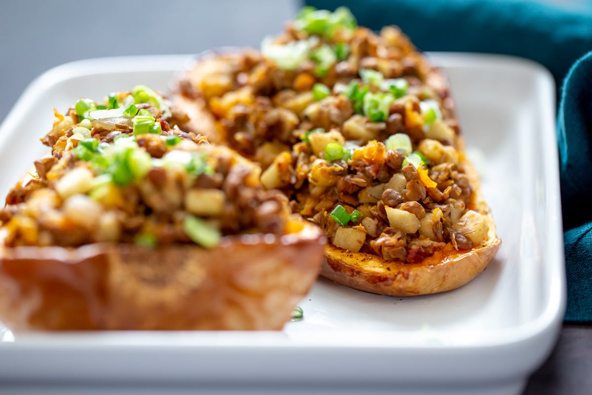 vegan stuffed butternut squash side view of two stuffed butternut squash halves in a casserole dish