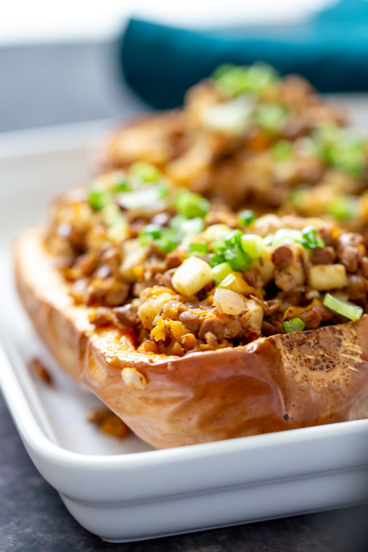 vegan stuffed butternut squash close-up of a lentil and apple stuffed baked butternut squash half in a white casserole dish