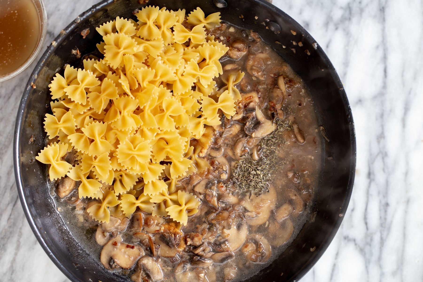 vegan mushroom stroganoff farfalle pasta being added to a pan with mushroom sauce