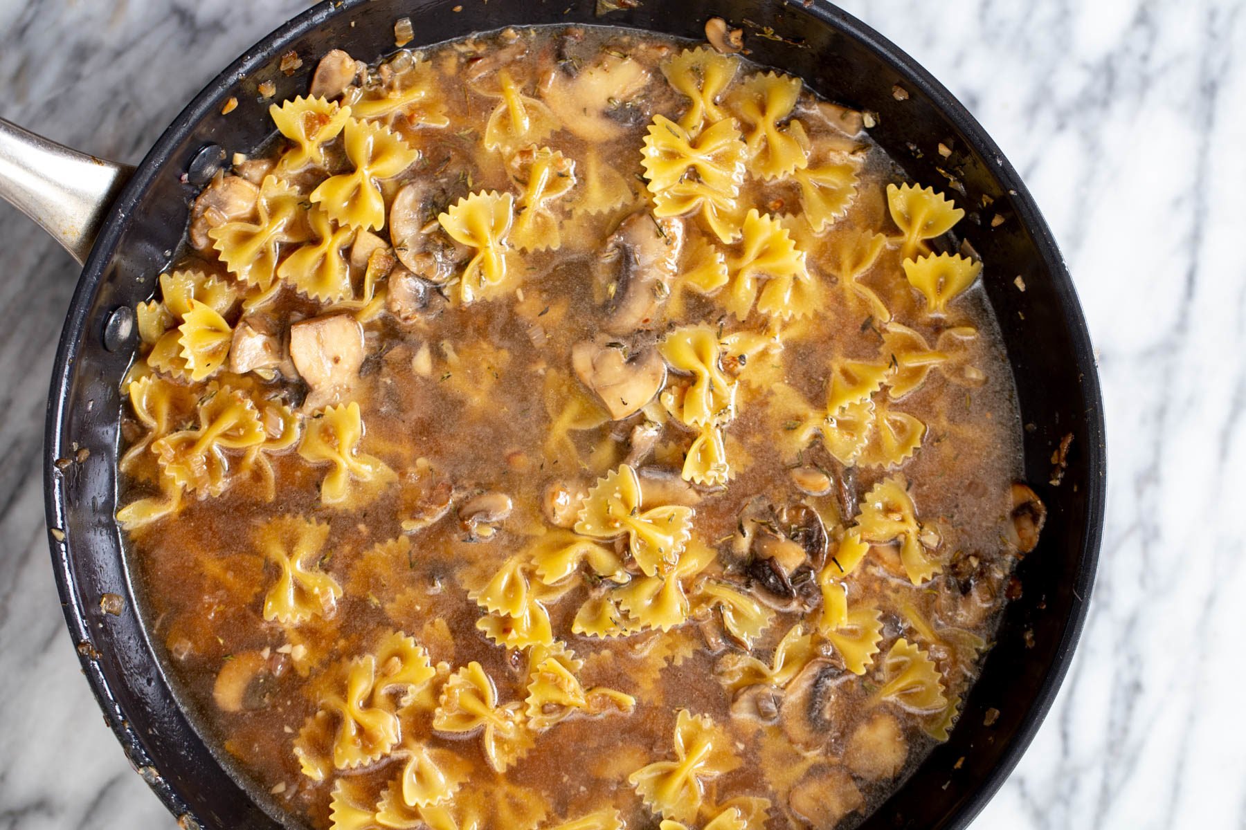vegan mushroom stroganoff uncooked farafalle pasta and mushroom sauce cooking in a saucepan