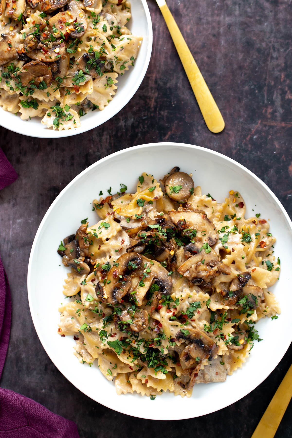 vegan mushroom stroganoff  overhead shot of two plates of vegan mushroom stroganoff served on farfalle topped with chopped parsley