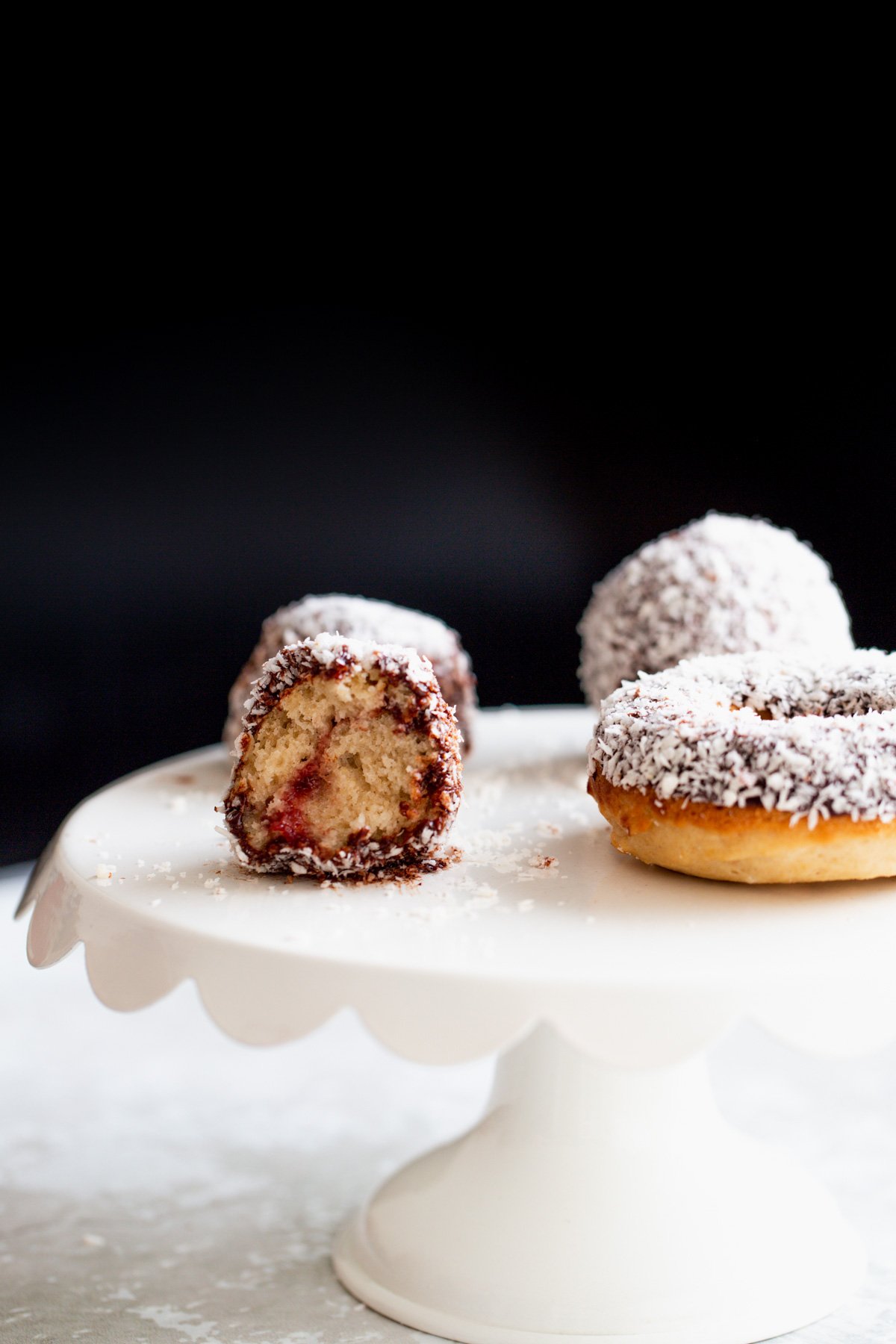 donut holes on a cake stand  side view of a vegan lamington donut hole with one bite taken