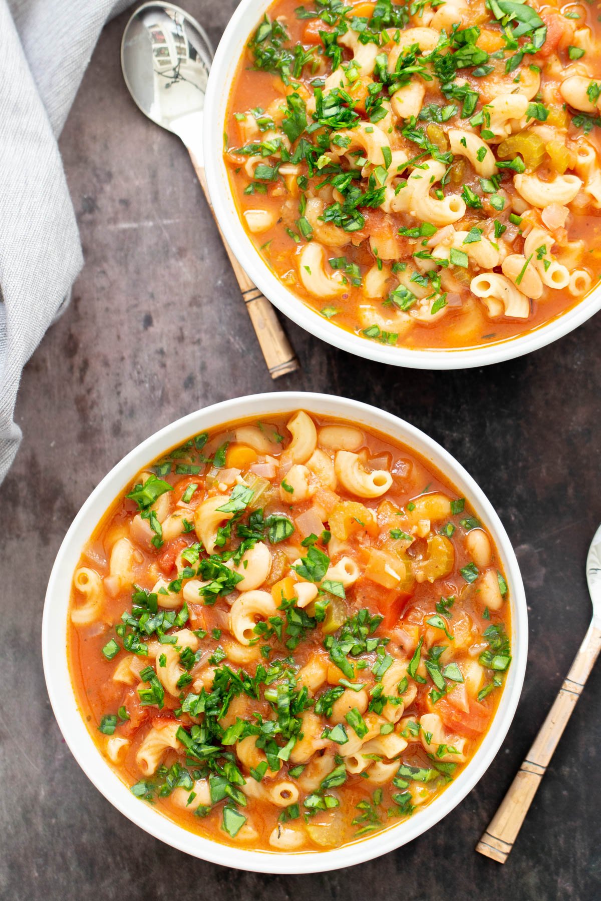two bowls filled with vegan pasta e fagioli white bean and pasta soup with spoons on the side