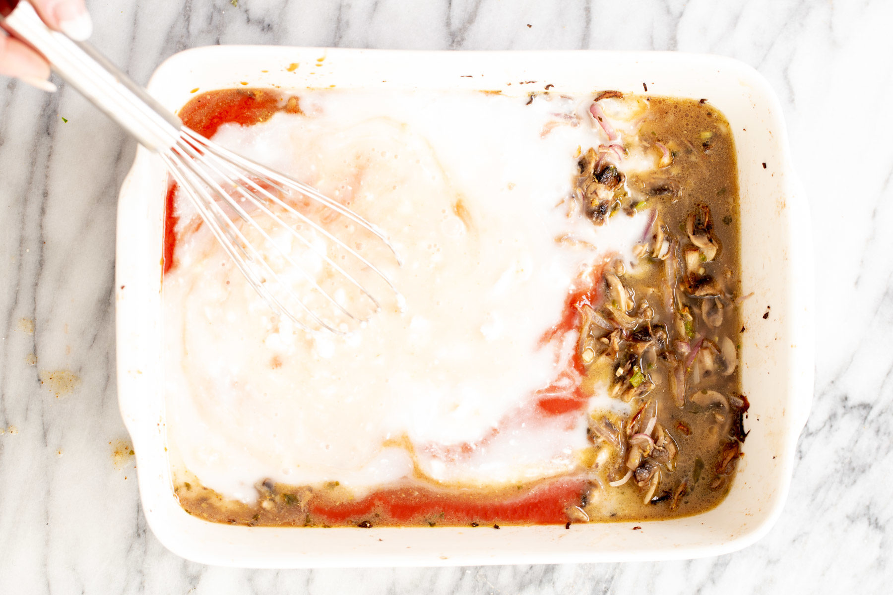 tomato puree and coconut milk being added to baked mushrooms and onion to make butter chicken lasagna