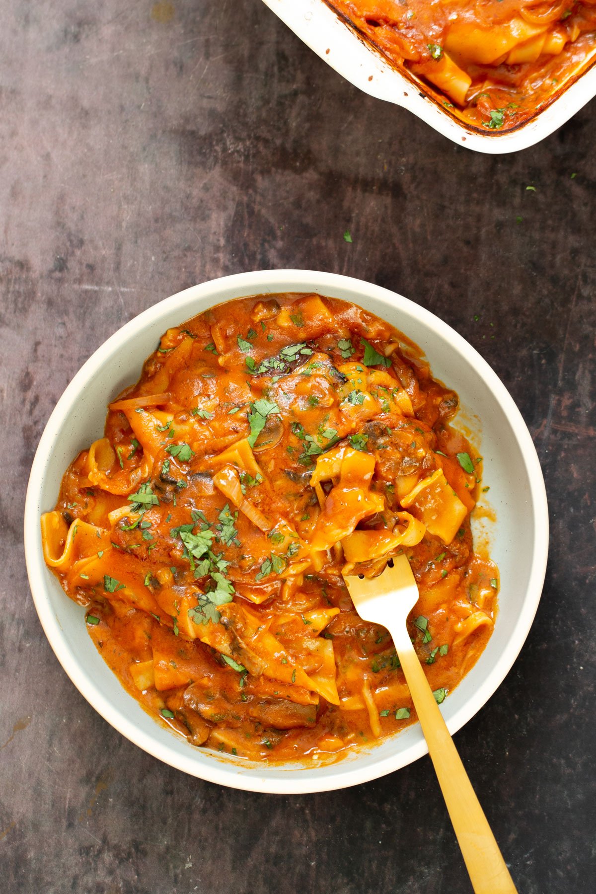 butter chicken lasagna a bowl filled with vegan butter chicken lasagna with a fork sticking in