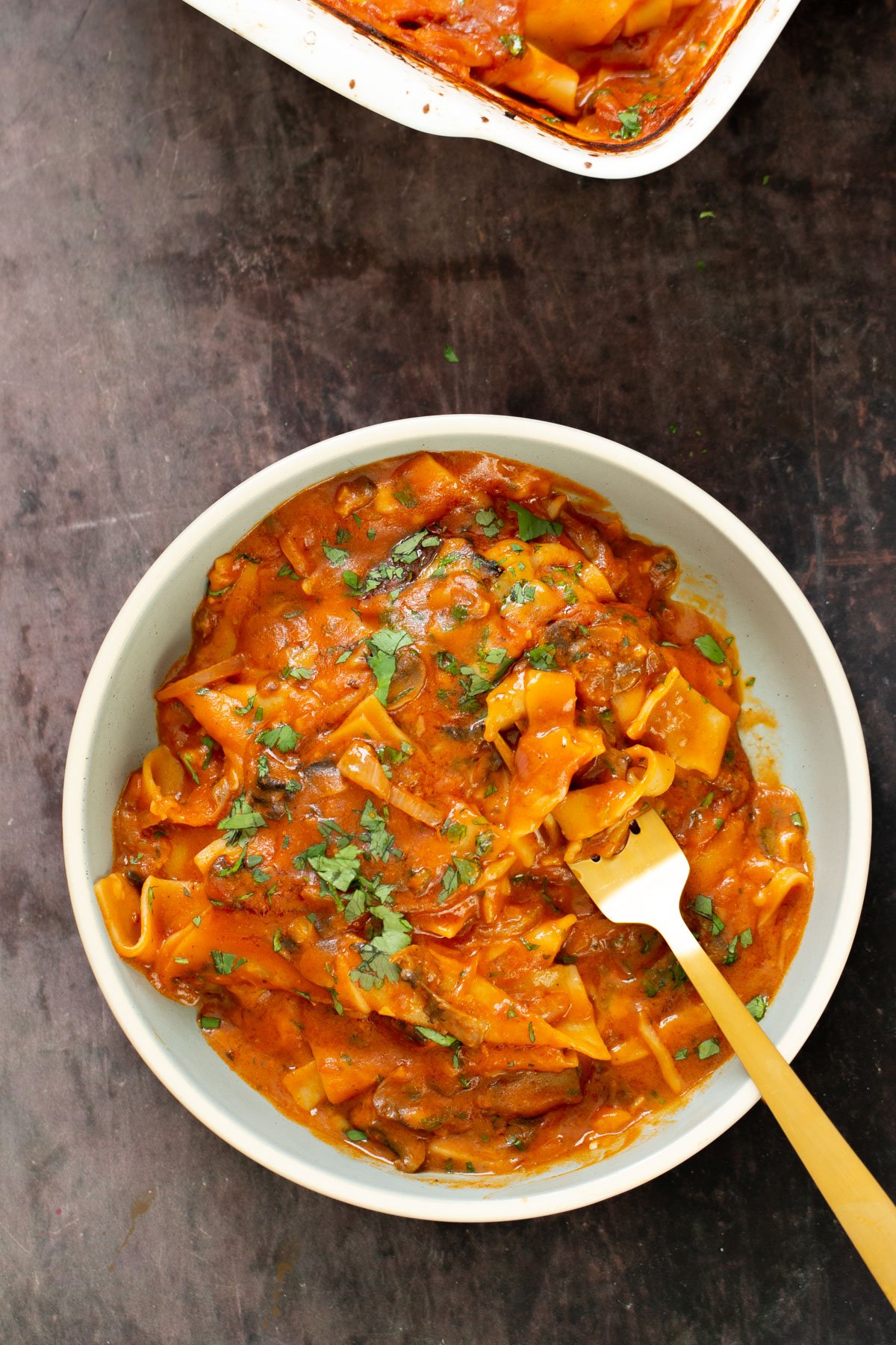 a serving of vegan butter chicken lasagna bake in a white bowl with a fork