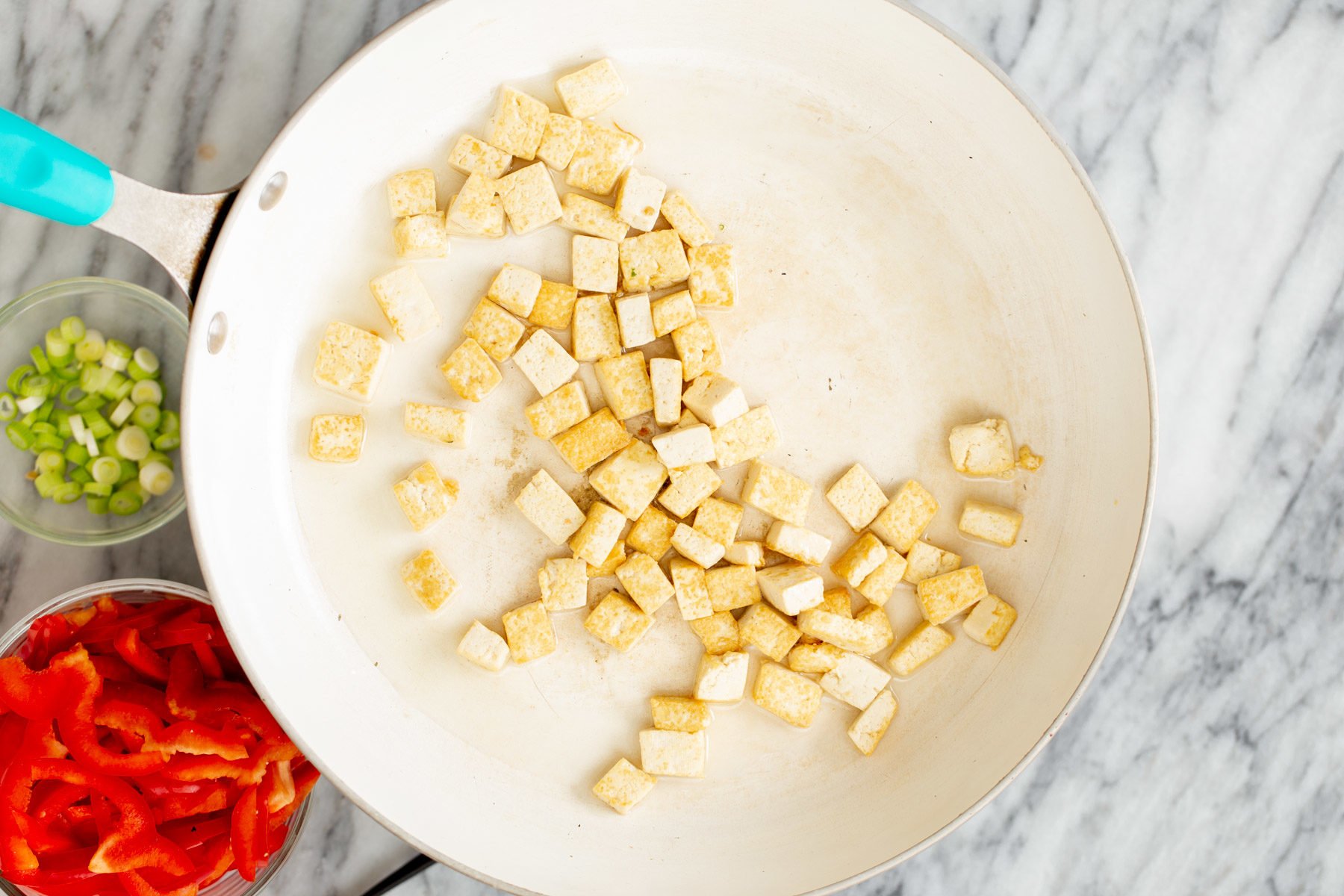 pressed tofu cubes being fried until golden in a white pan