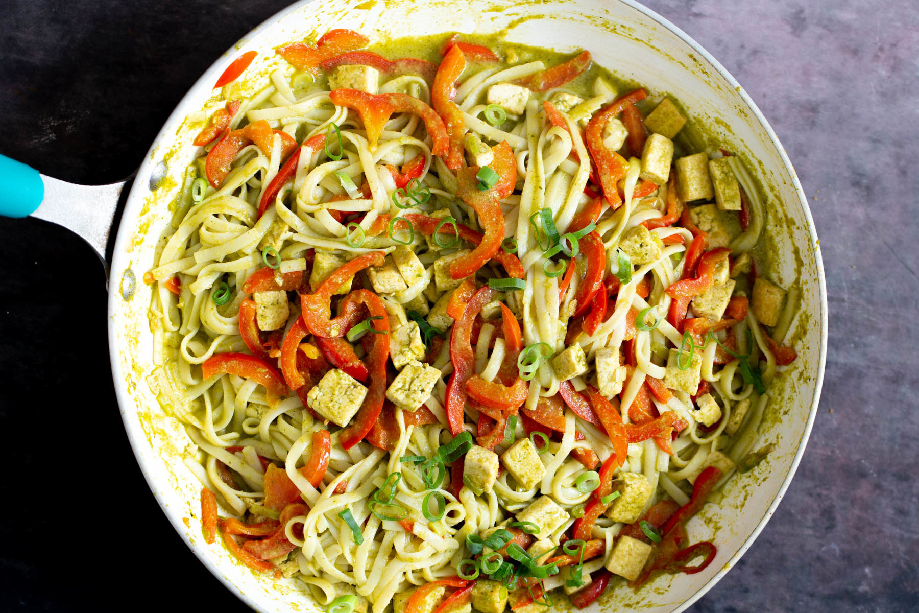 Thai Green Curry Sauce rice noodles being tossed in a pan with sauteed veggies, tofu and green curry sauce