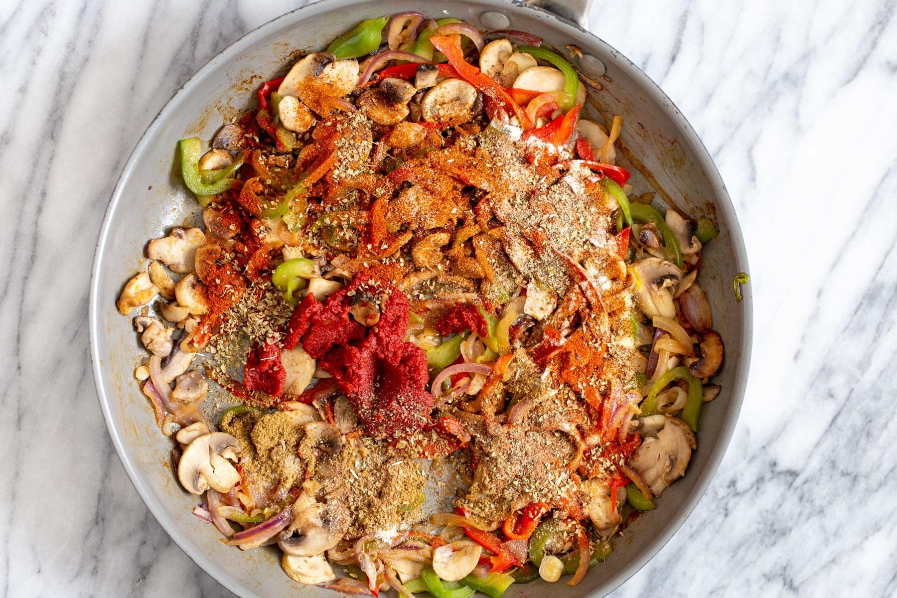 vegan tostadas Mexican spices and tomato paste being added to veggies in a pan