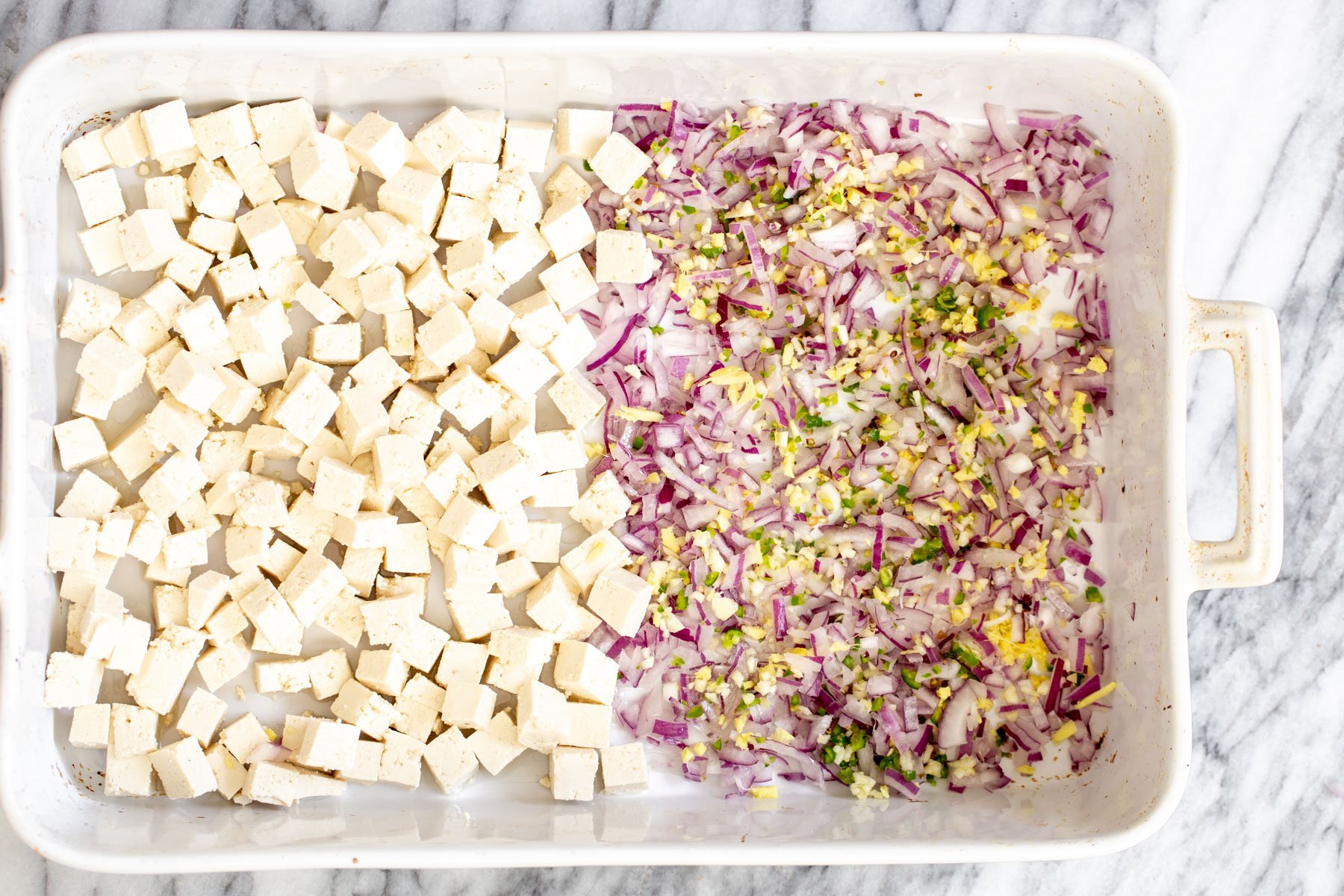 baked tofu curry  tofu cubes in a casserole dish next to minced onion, ginger, garlic and chile