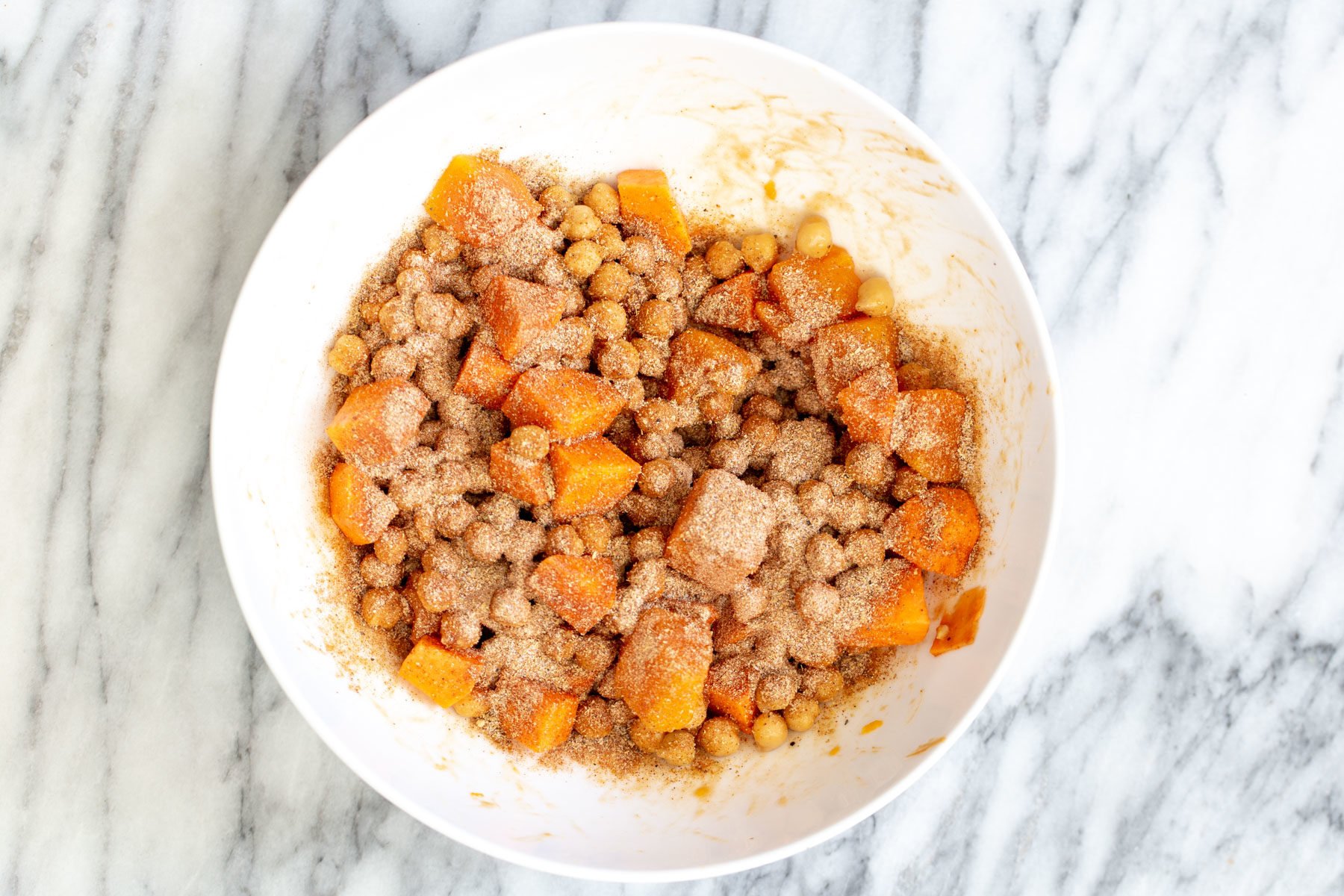 spice mix being sprinkled on top of sweet potatoes and chickpeas