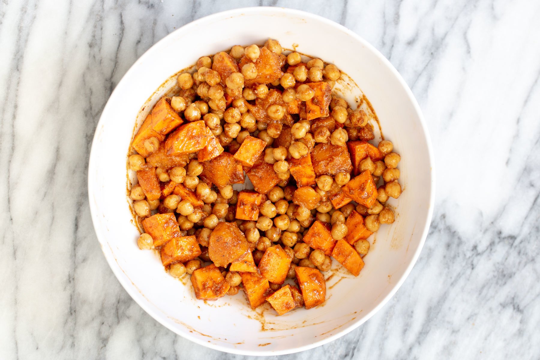 sweet potato cubes and chickpeas being mixed with a blend of spices