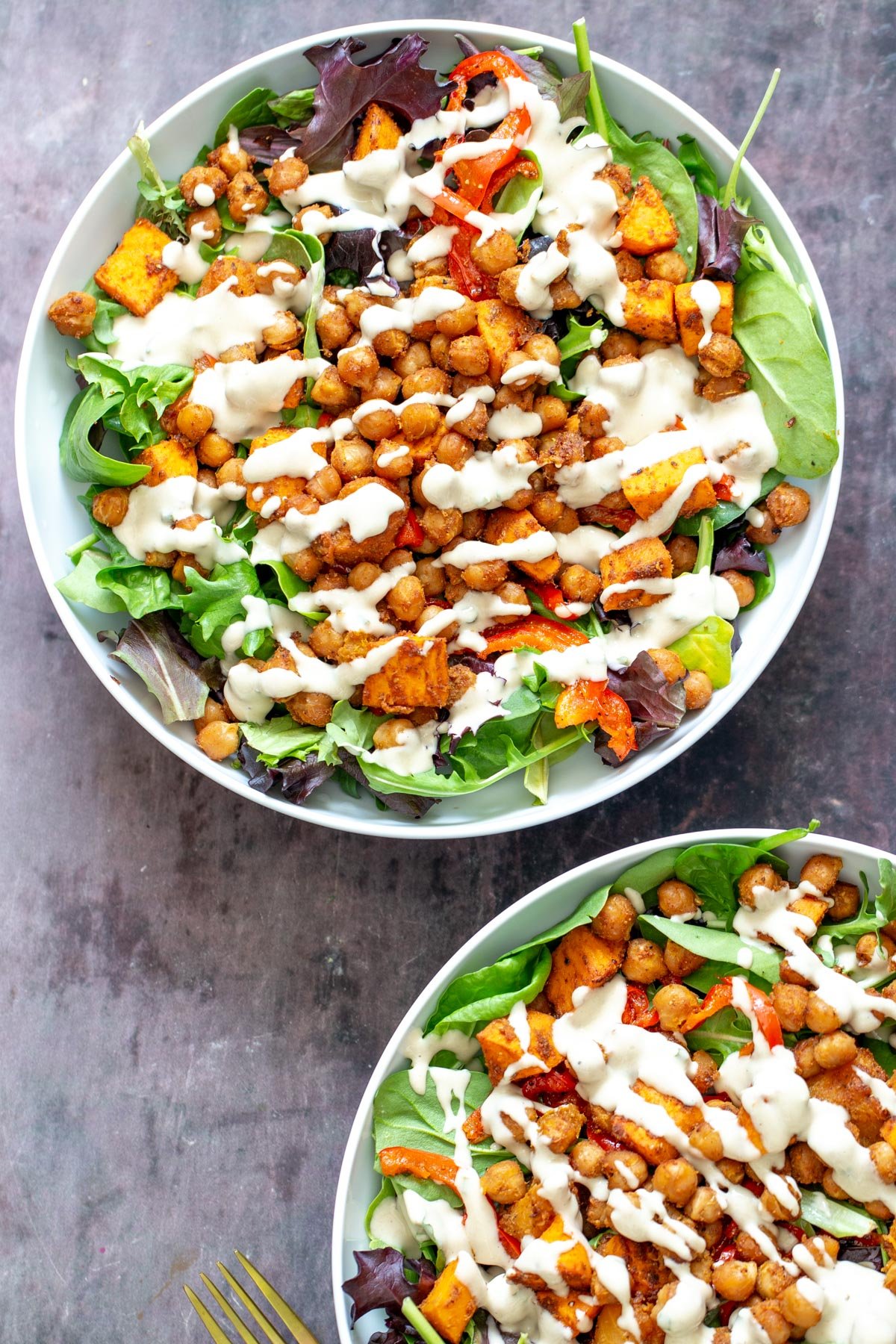 sweet potato chickpea salad  two salad bowls with spring mix topped with roasted chickpeas, bell peppers and sweet potatoes and tahini dressing