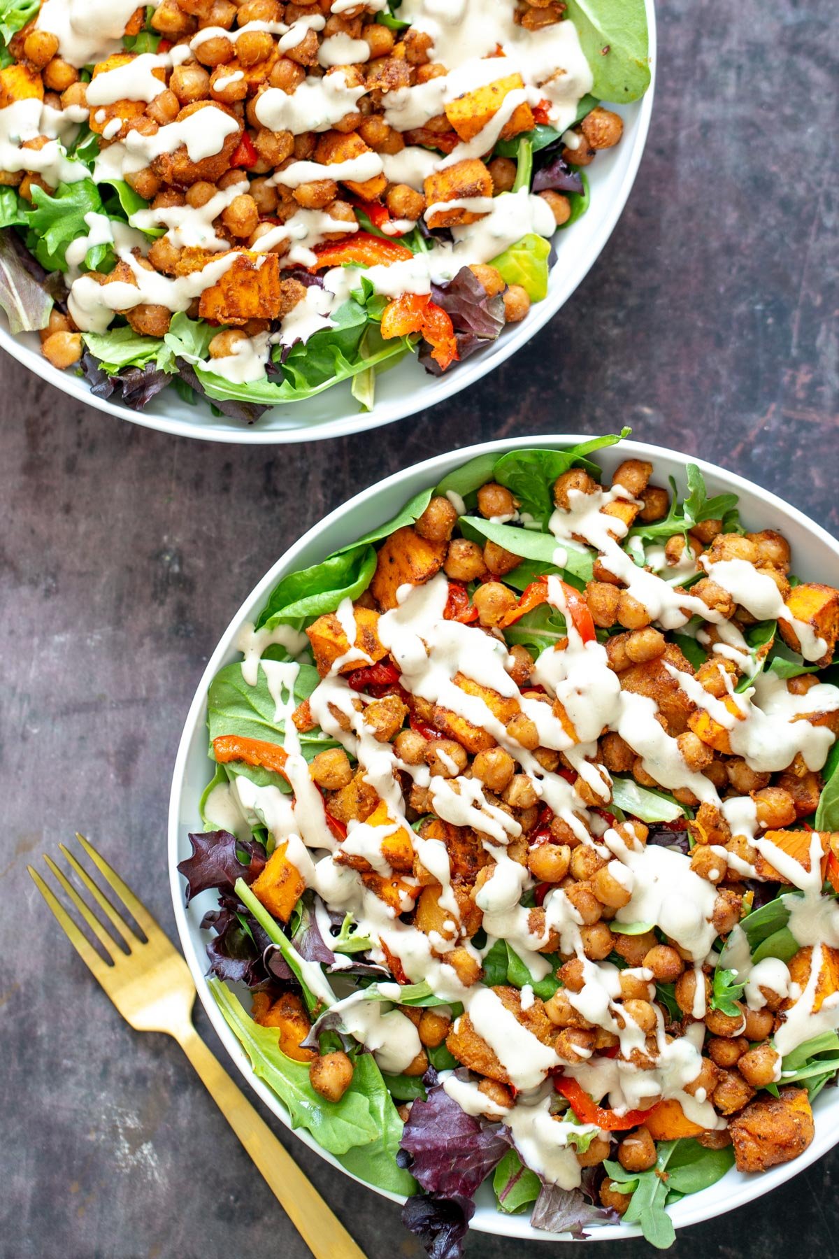 sweet potato salad  two bowl with leafy greens topped with roasted chickpeas and cubed sweet potato