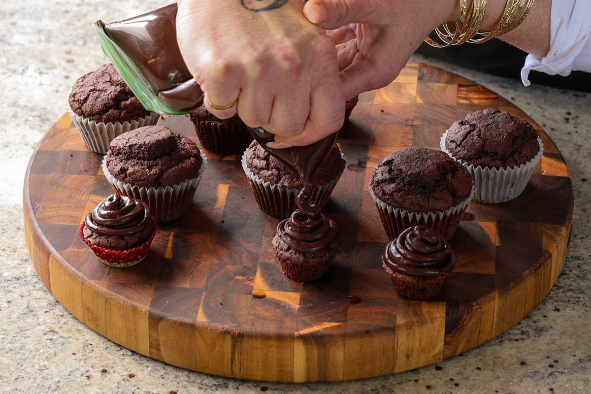 piping chocolate ganache frosting onto the gluten-free chocolate cupcakes