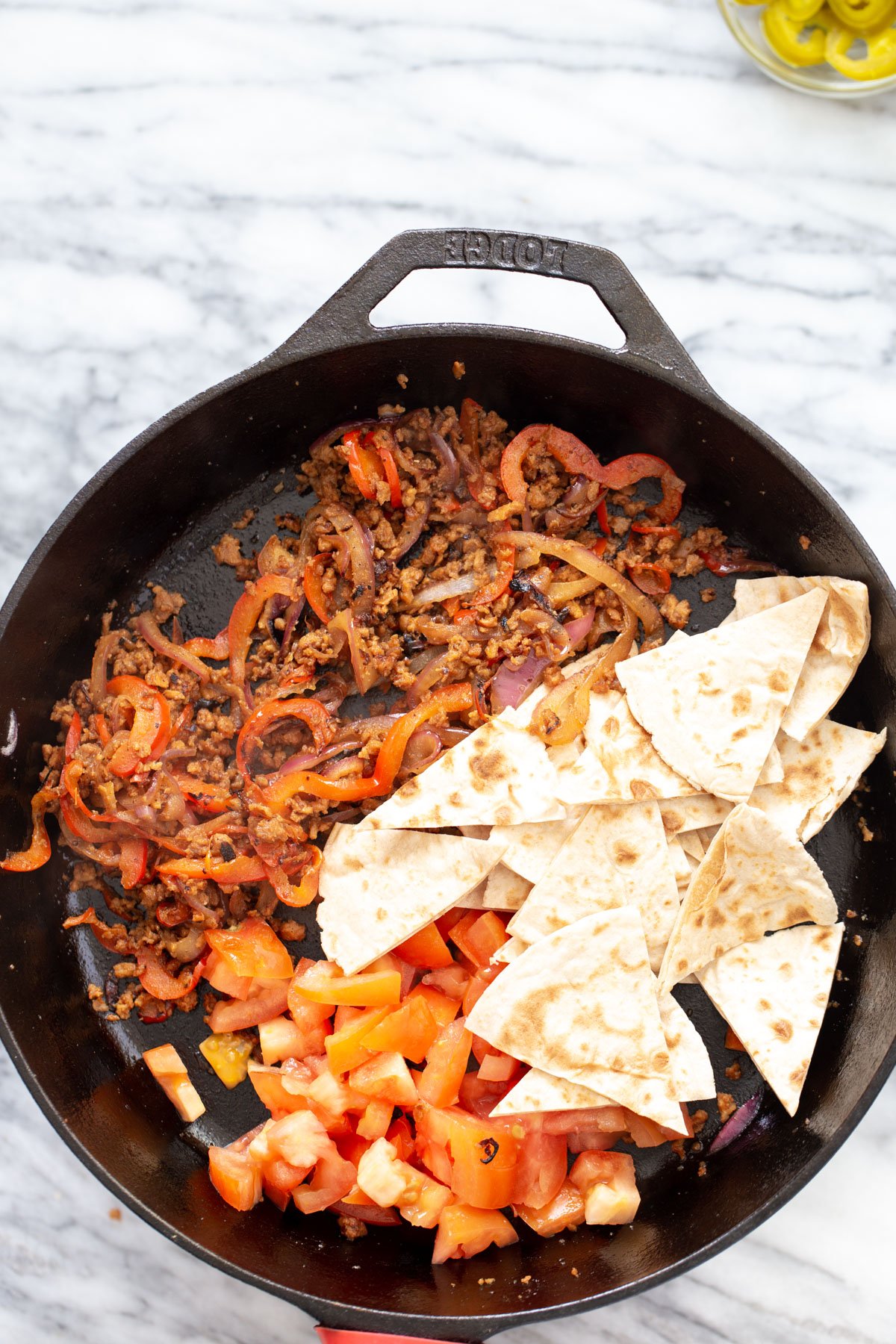 tortillas and chopped tomatoes being added to skillet with veggie crumble mix