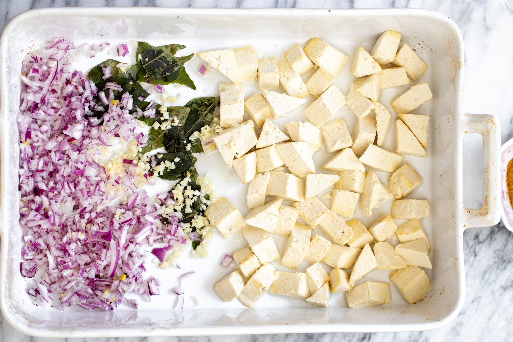 tofu casserole a casserole dish with cubed tofu, chopped onions and curry leaves