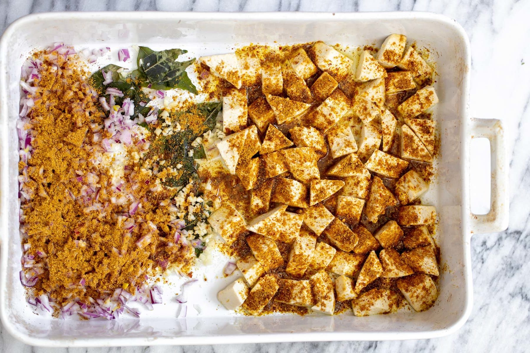 tofu, onions and curry leaves in a casserole dish sprinkled with madras curry powder