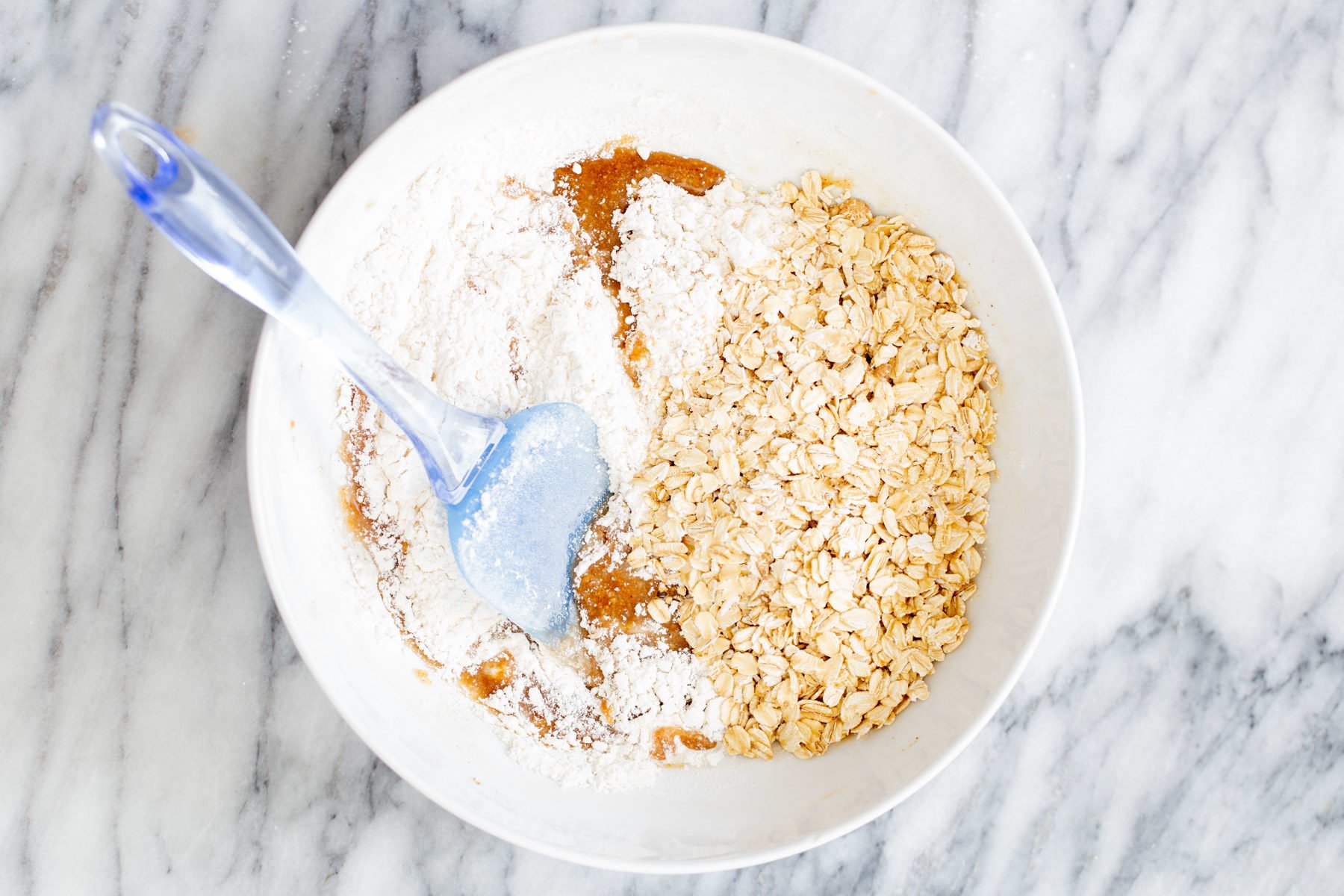 oats and flour being added to wet dough to make vegan oatmeal bars 