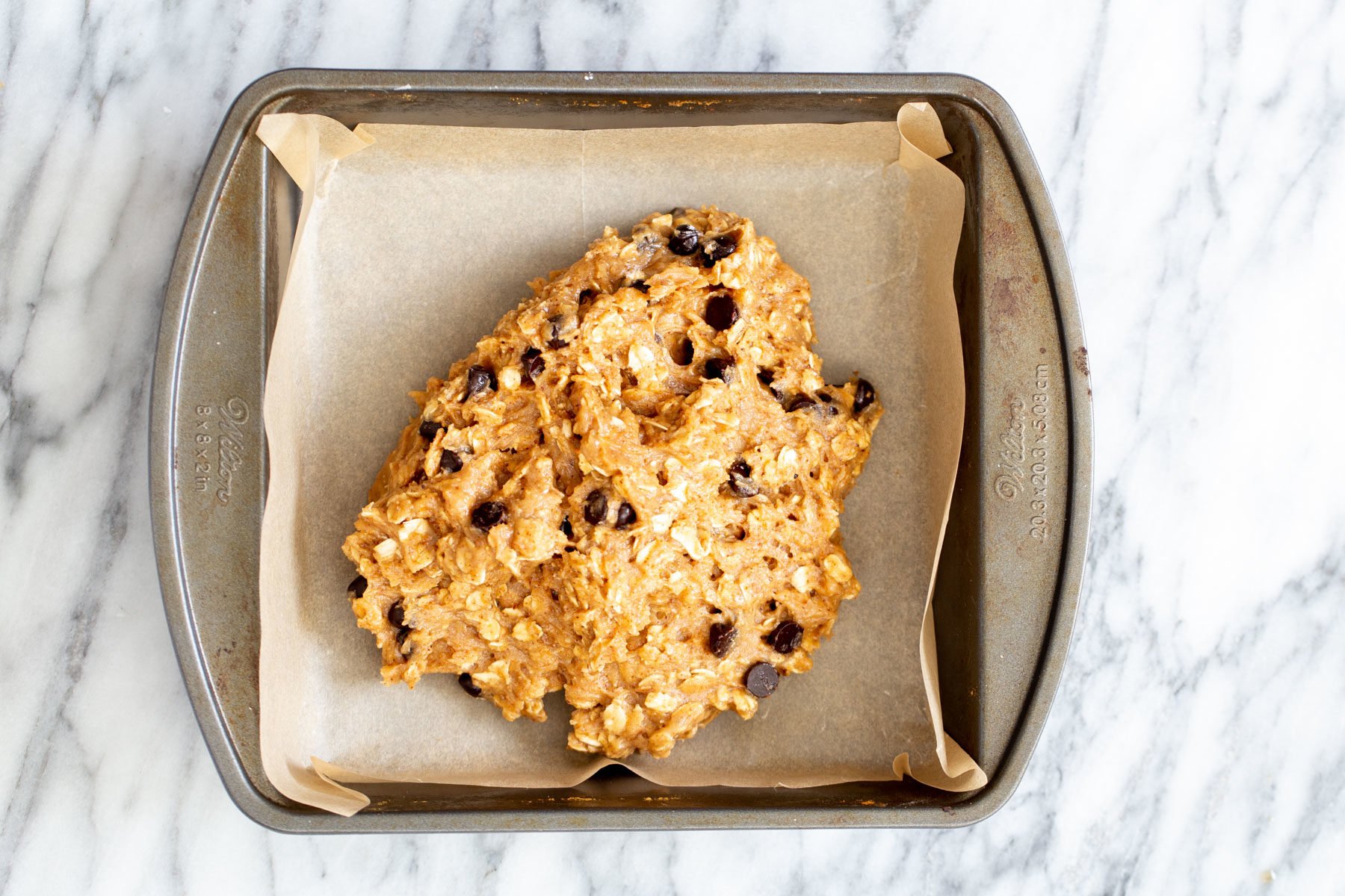 vegan date caramel oatmeal bar batter being added to a square baking pan 