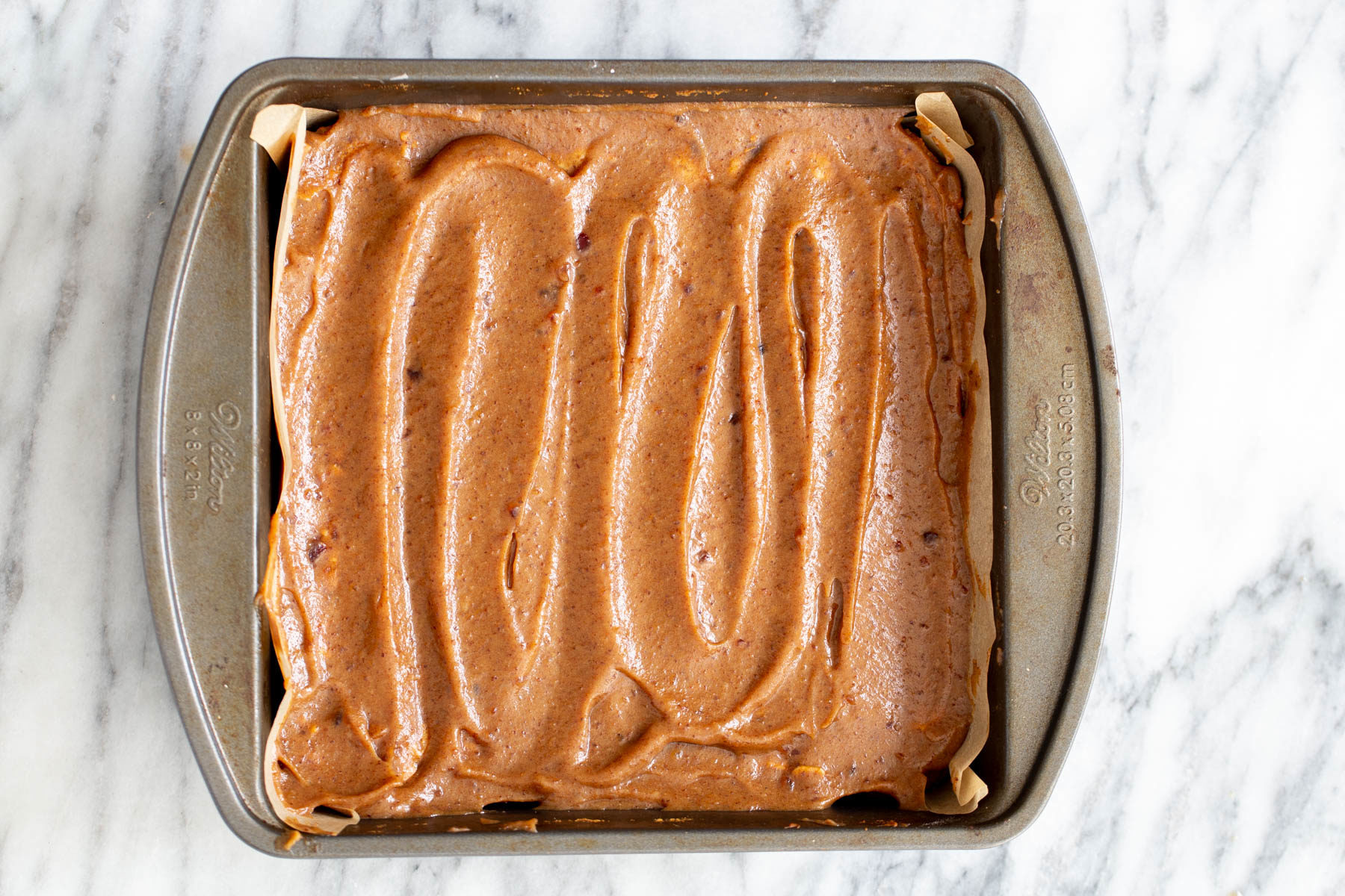 vegan date caramel being spread on oatmeal batter to make vegan date caramel oatmeal bars 