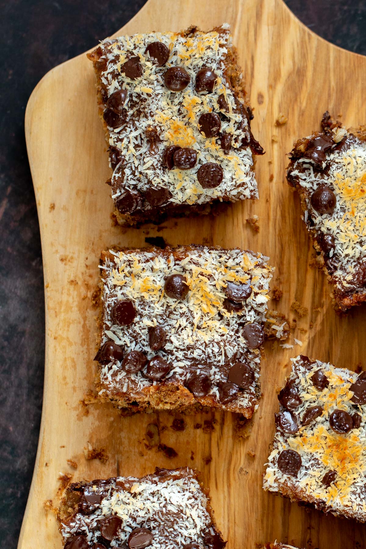vegan oatmeal date caramel snack bars topped with shredded coconut and chocolate chips on a cutting board 