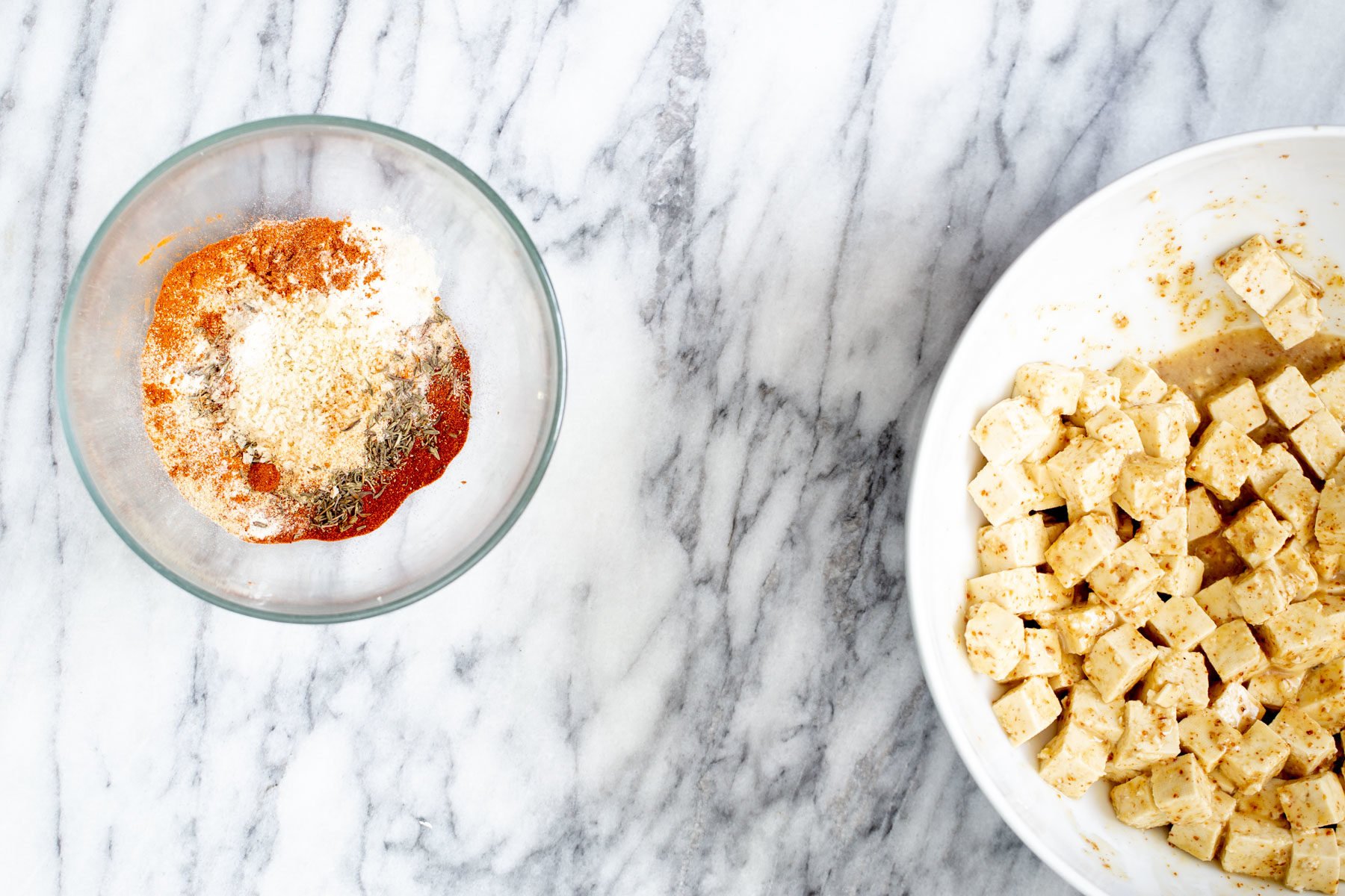 a bowl with marinated tofu and a bowl with spice mix on a marble countertop