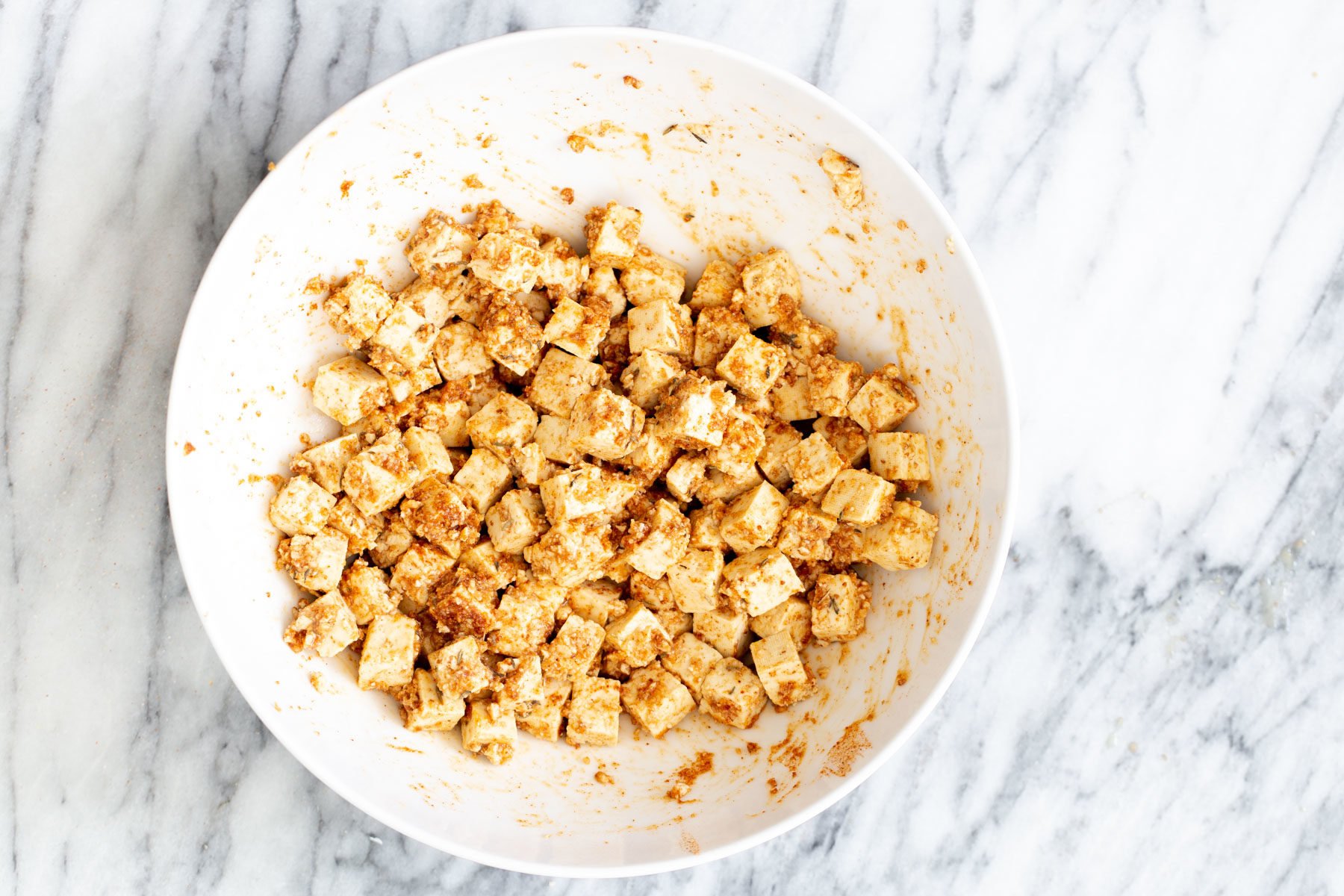 marinated cubed tofu being mixed with crunch topping