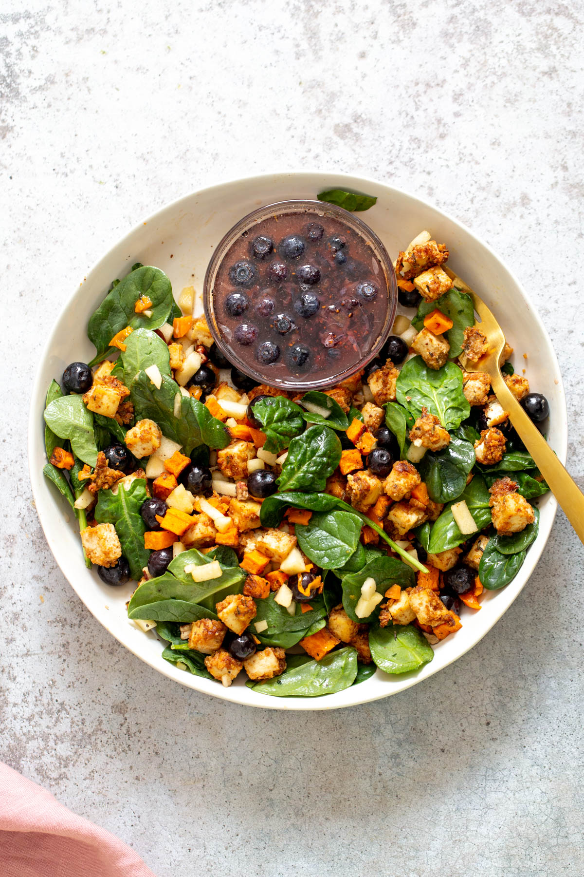 sweet potato tofu bowl a bowl with baby spinach topped with baked sweet potatoes and crunchy tofu served with a small dish of maple blueberry dressing