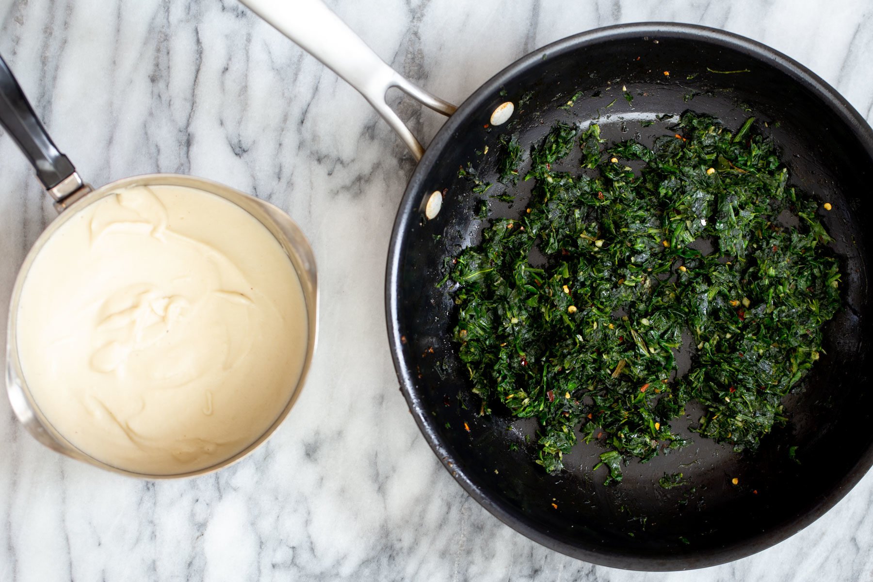 a pan with sauteed spinach next to a saucepan with vegan mozzarella cheese spread