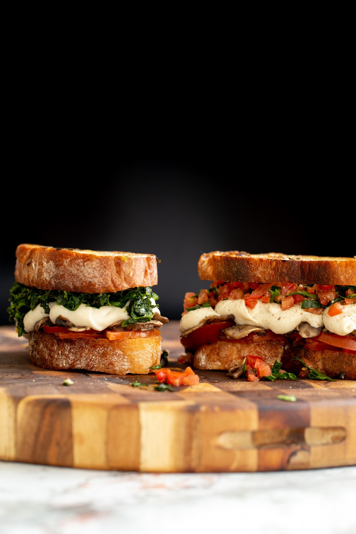 two homemade vegan mozzarella cheese melts with spinach and mushrooms on a wooden board