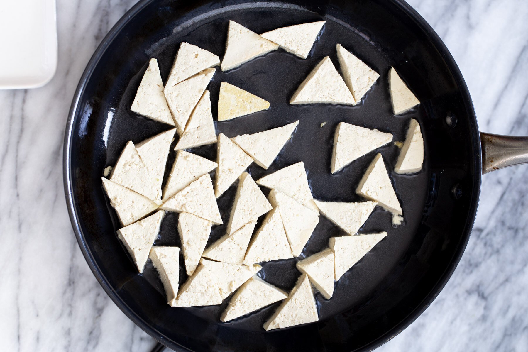 pressed tofu triangles being added to a black skillet