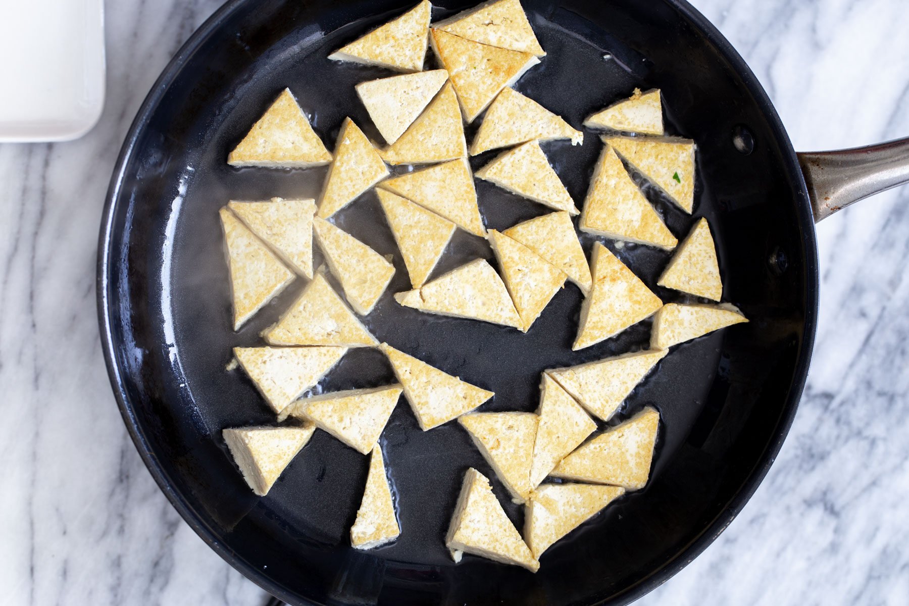 pan-fried tofu triangles in a cast-iron skillet