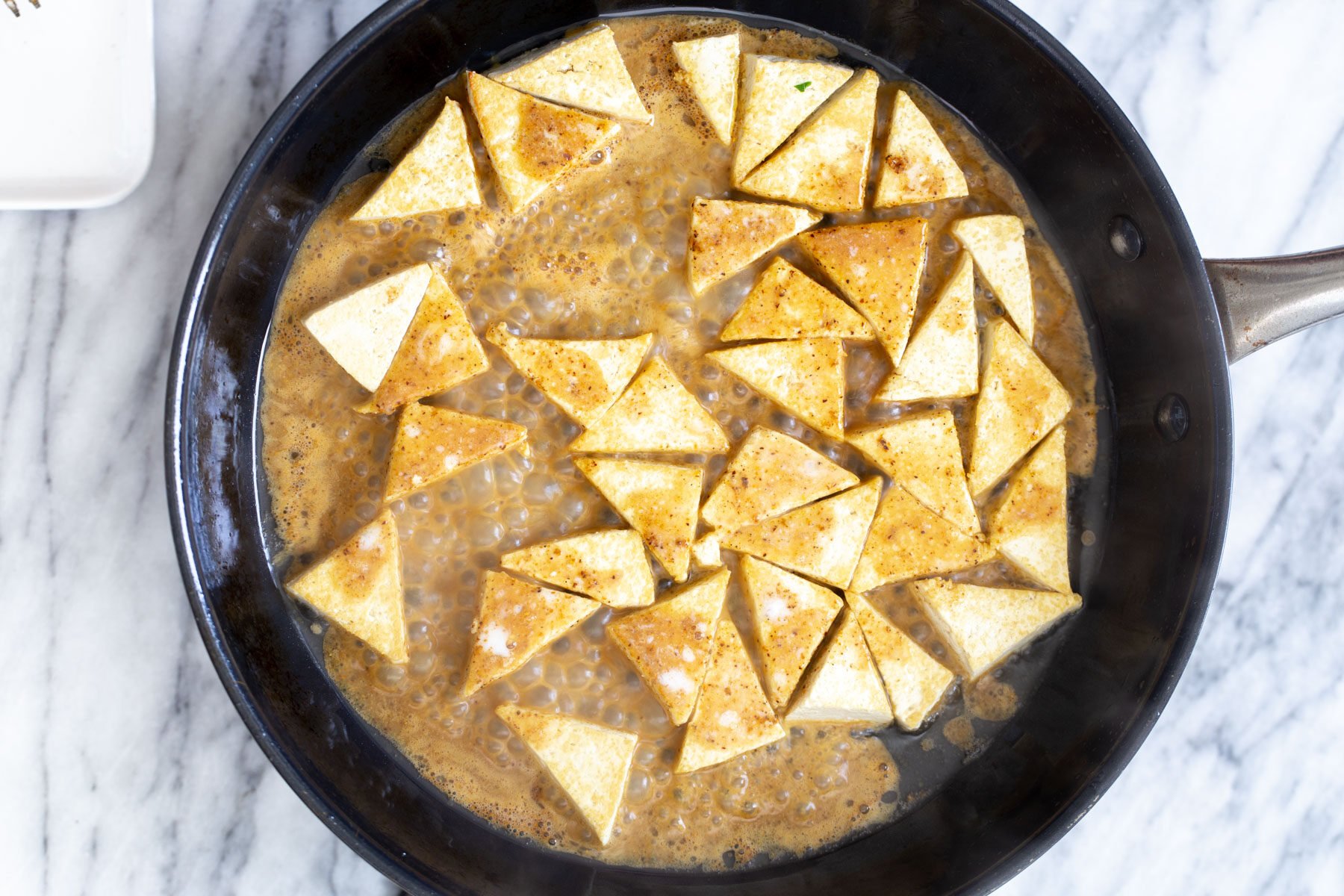 curry sauce being added to saucepan to coat pan-fried tofu
