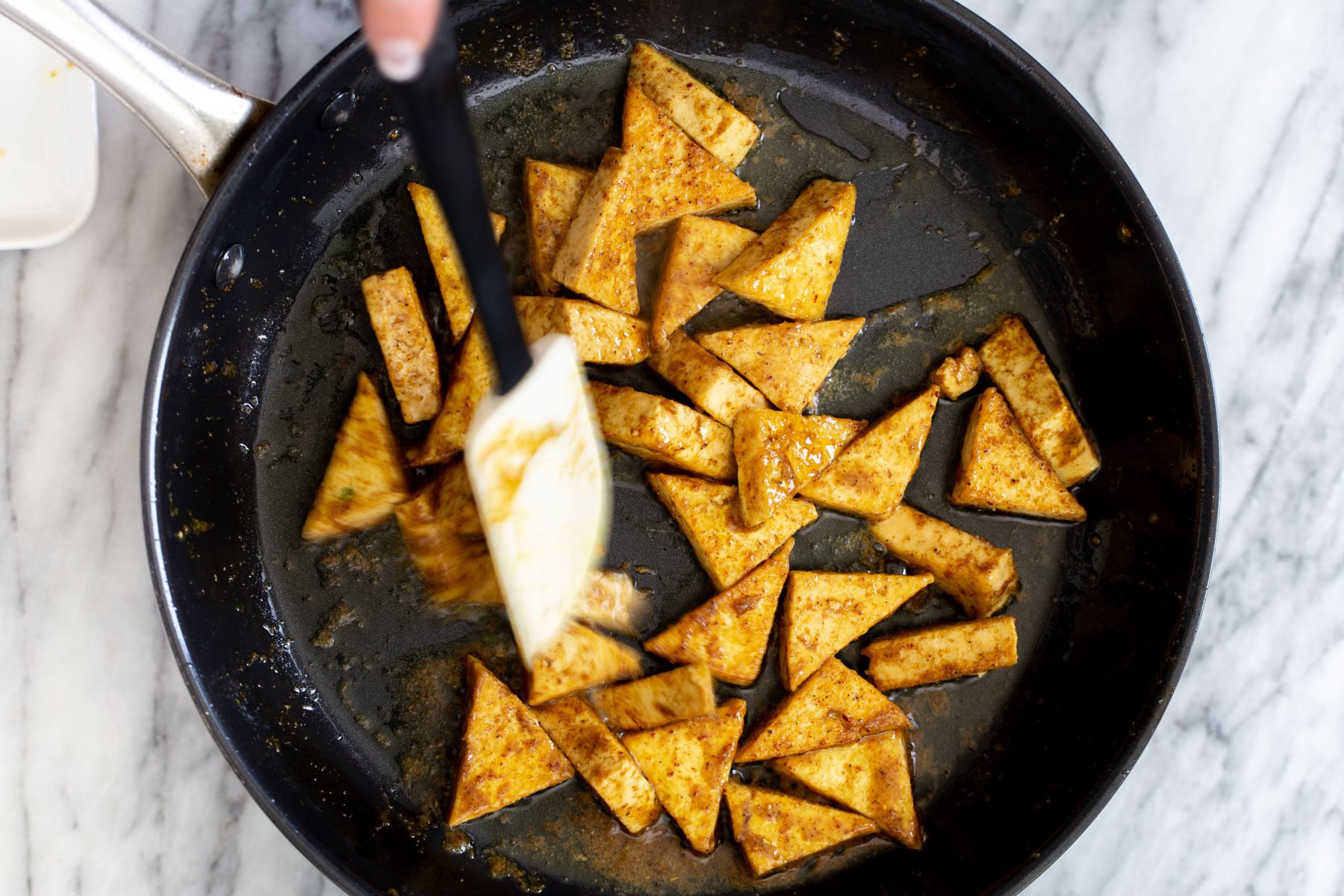 pan-fried tofu being tossed in curry sauce in a black skillet