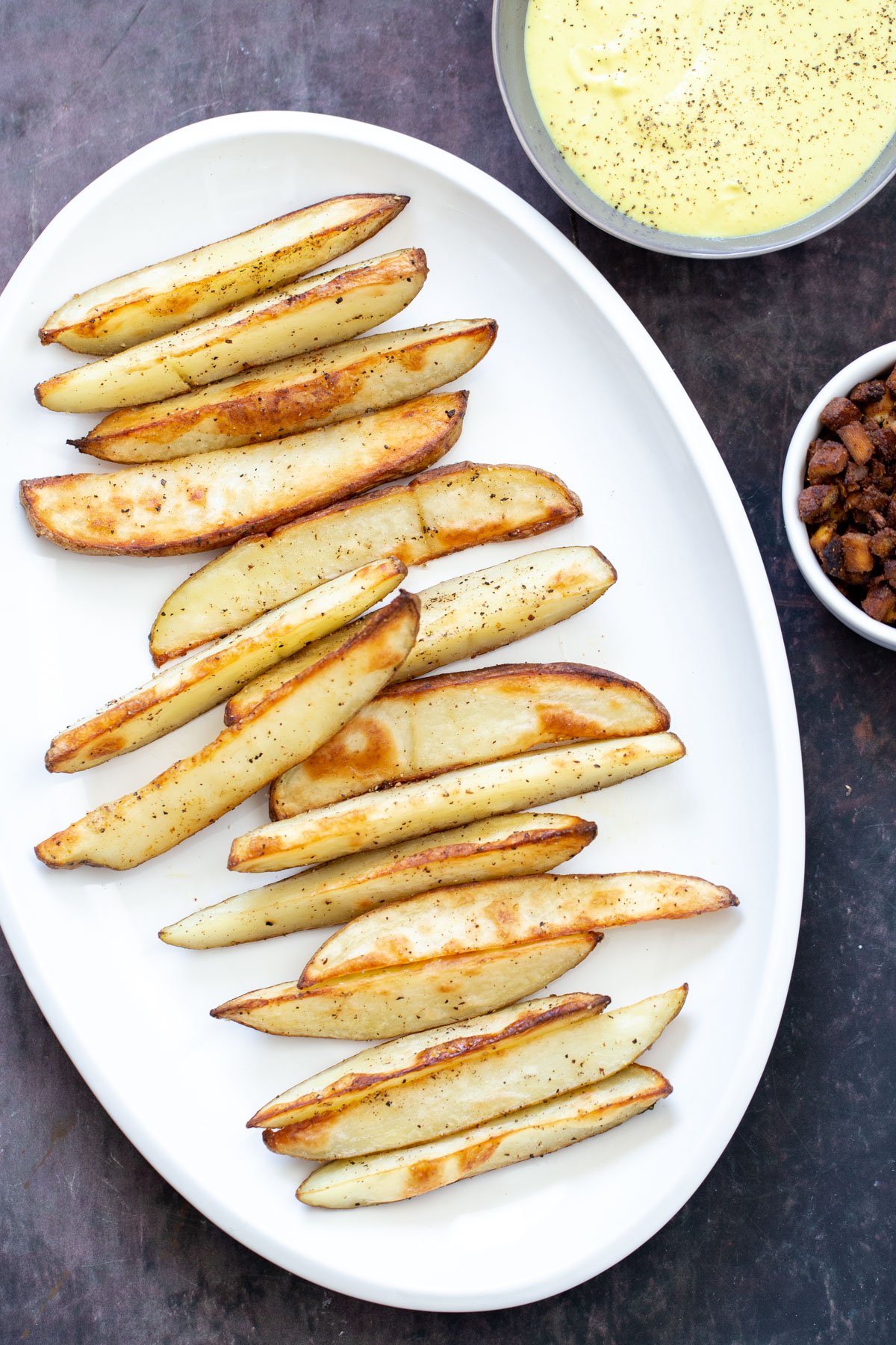 loaded potato wedges  a platter of crispy vegan baked potato wedges next to a small bowl of queso and tofu bacon