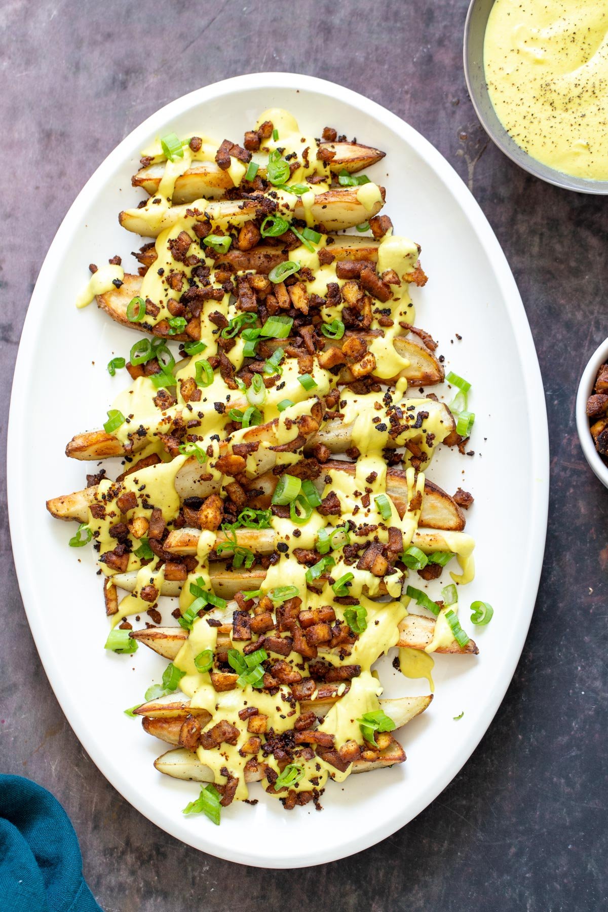 loaded potato wedges  loaded baked potato wedges on a a platter topped with vegan cheese sauce and tofu bacon