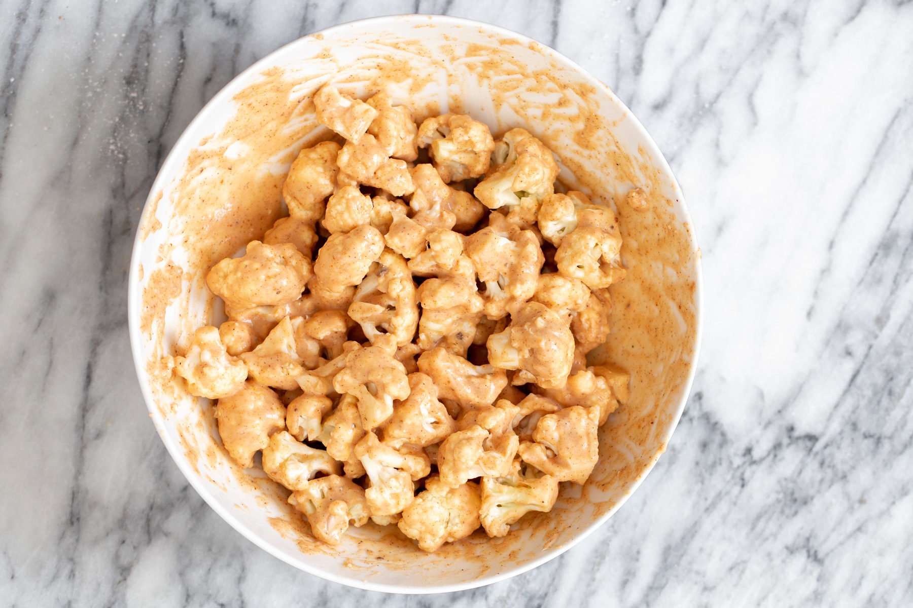 cauliflower florets being tossed in spiced beer batter to make vegan wings