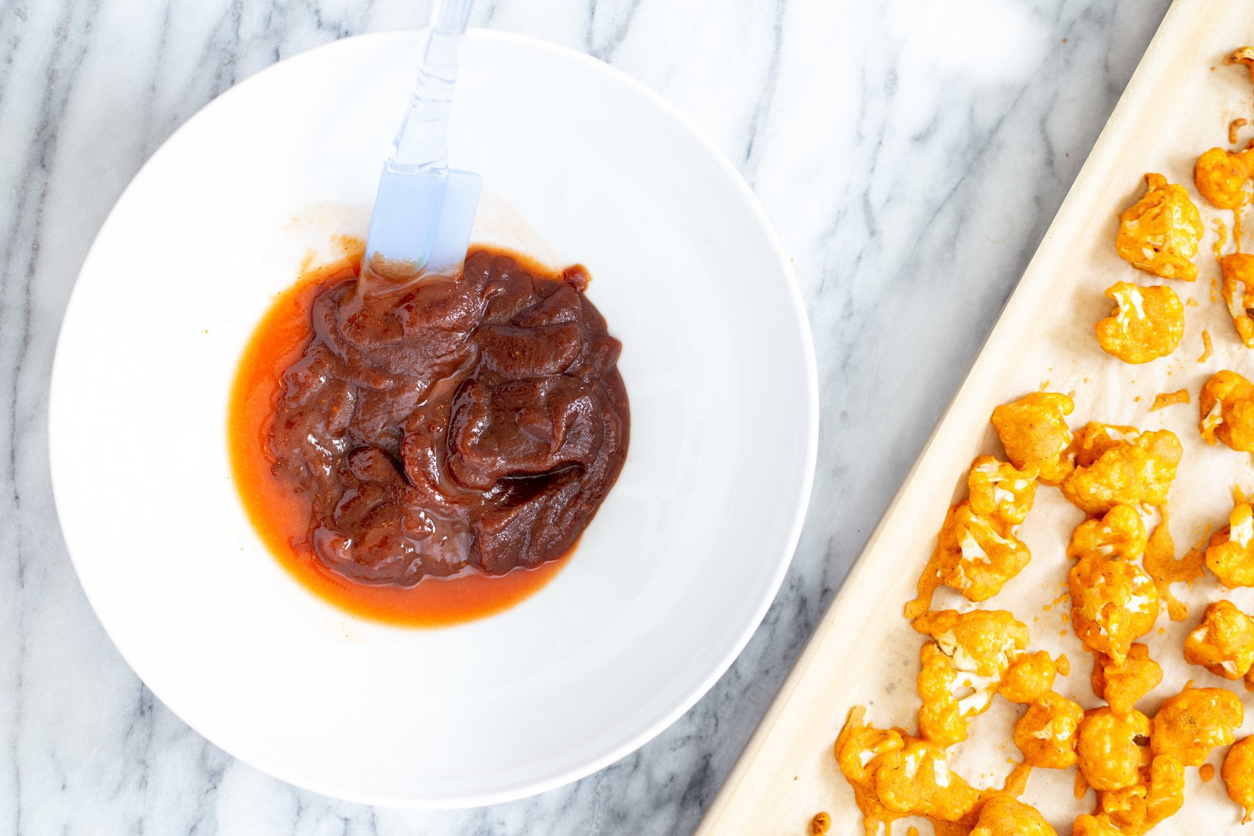 cauliflower wings  hot sauce and bbq sauce being mixed in a small dish