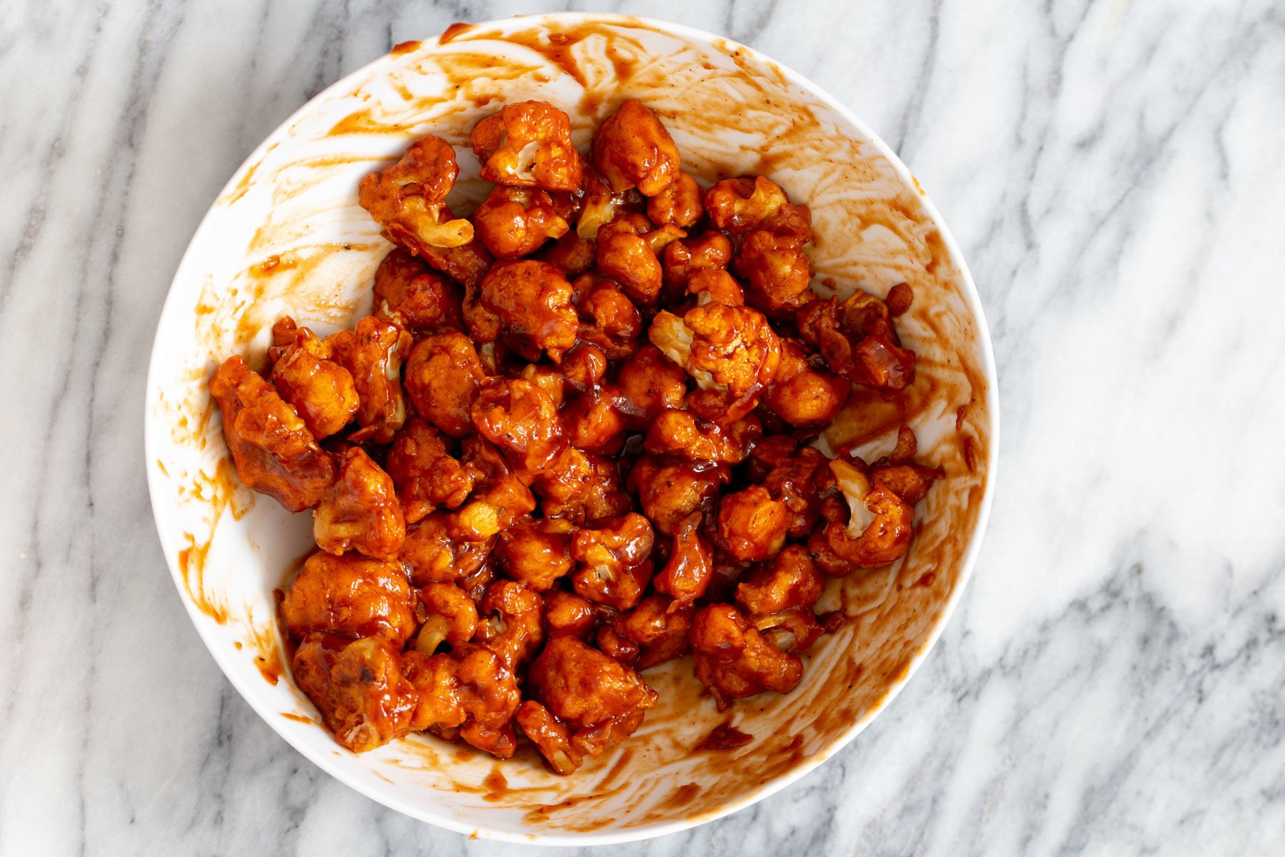 cauliflower wings  baked cauliflower wings being tossed in a small bowl with spicy bbq sauce